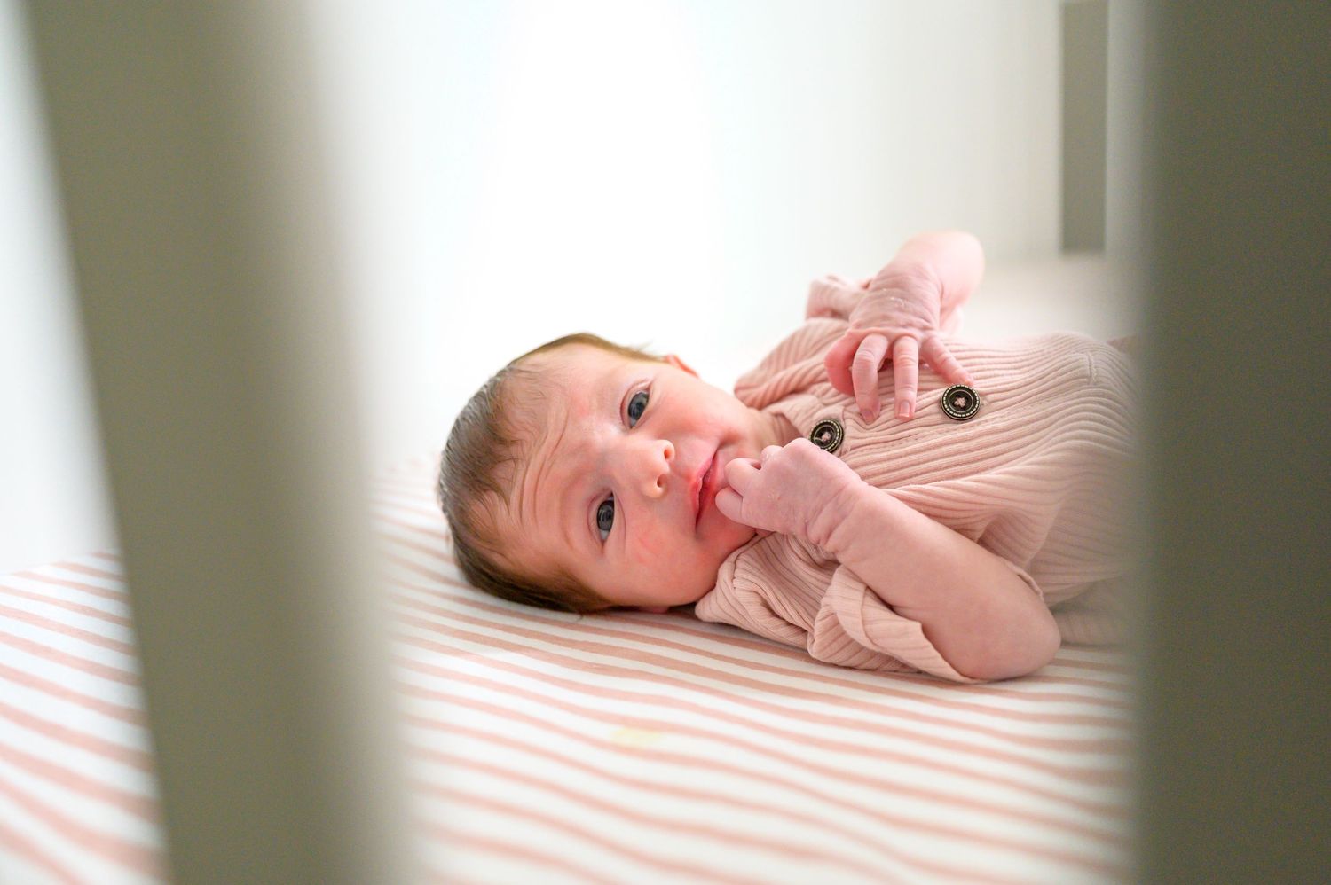 Photo of newborn little girl dressed in pink, laying awake in her crib