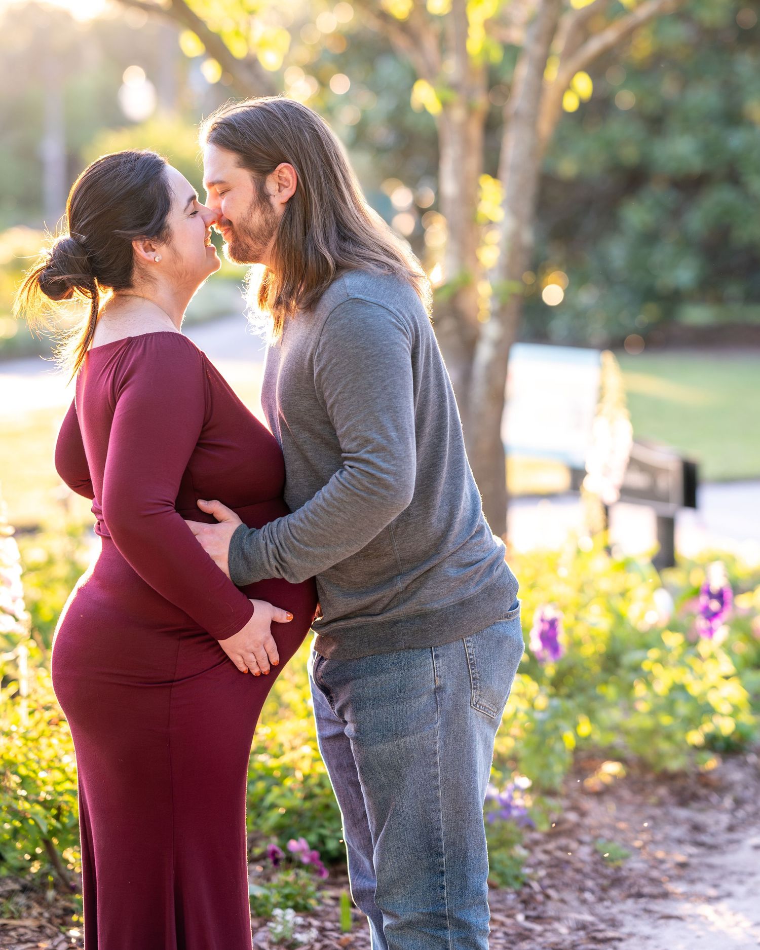 A couple embraces during a sunset photoshoot in a garden with golden light filtering through trees.