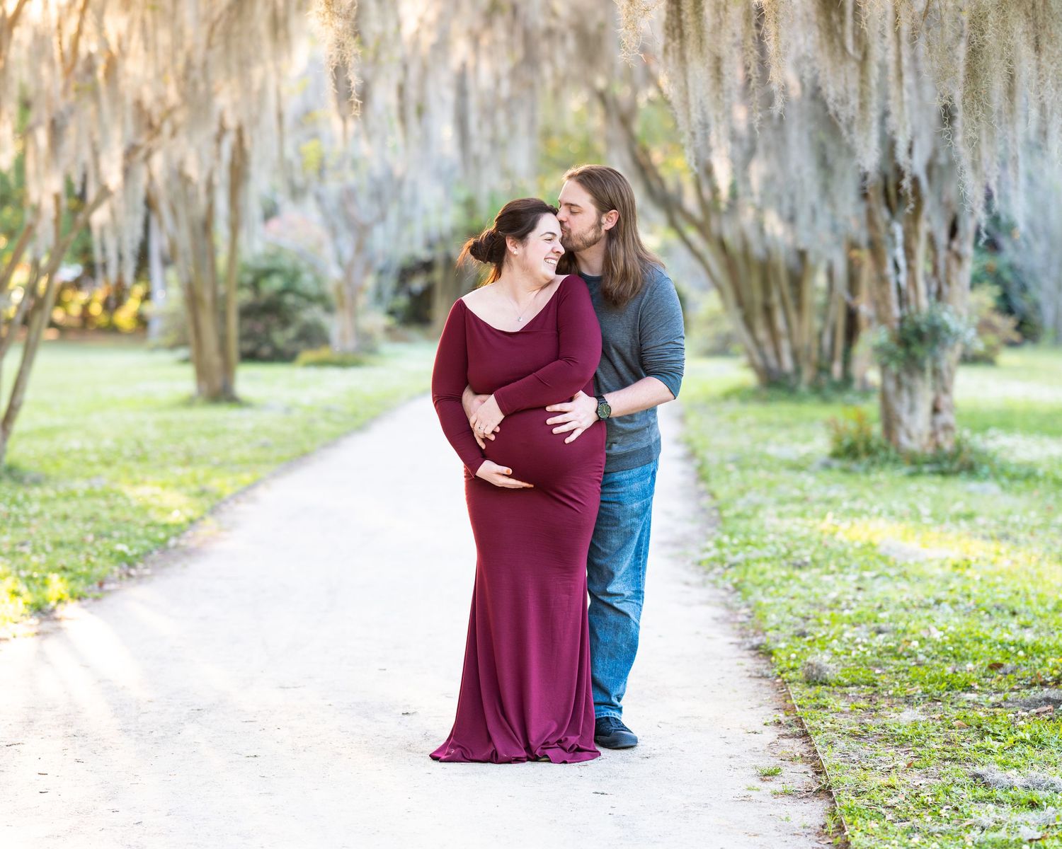 Couple embracing on garden path with Spanish moss hanging from trees.