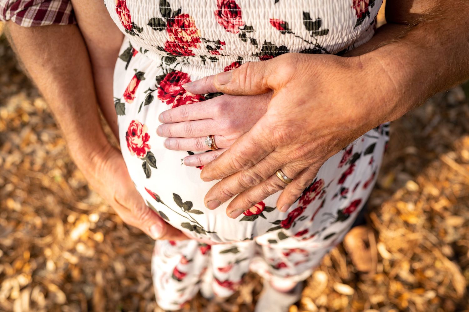 Close up photo of a woman's pregnant belly with her and her husband's ring hands on top of it