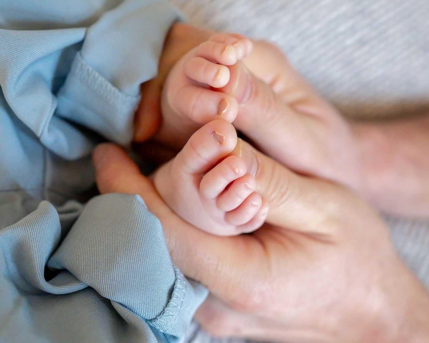 A  close-up photo showing gentle hand holding baby's feet with the baby's toes wrapped around his father's thumbs