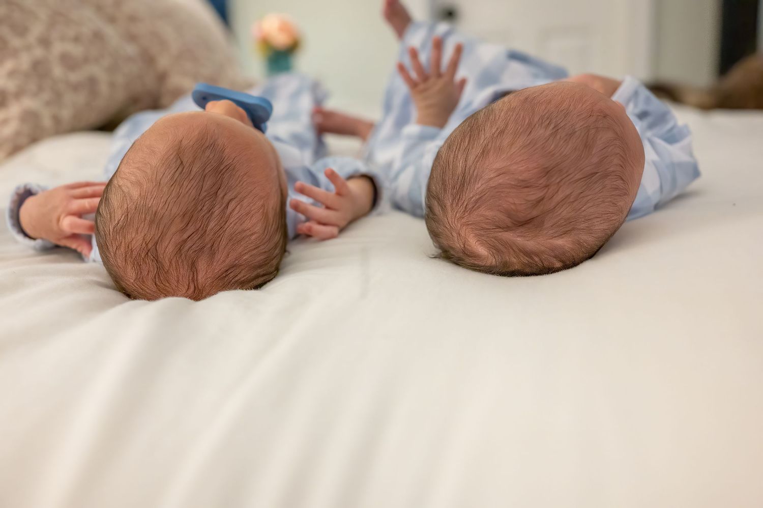 Twin newborn babies in matching blue outfits lying side by side on white bedding showing only their heads