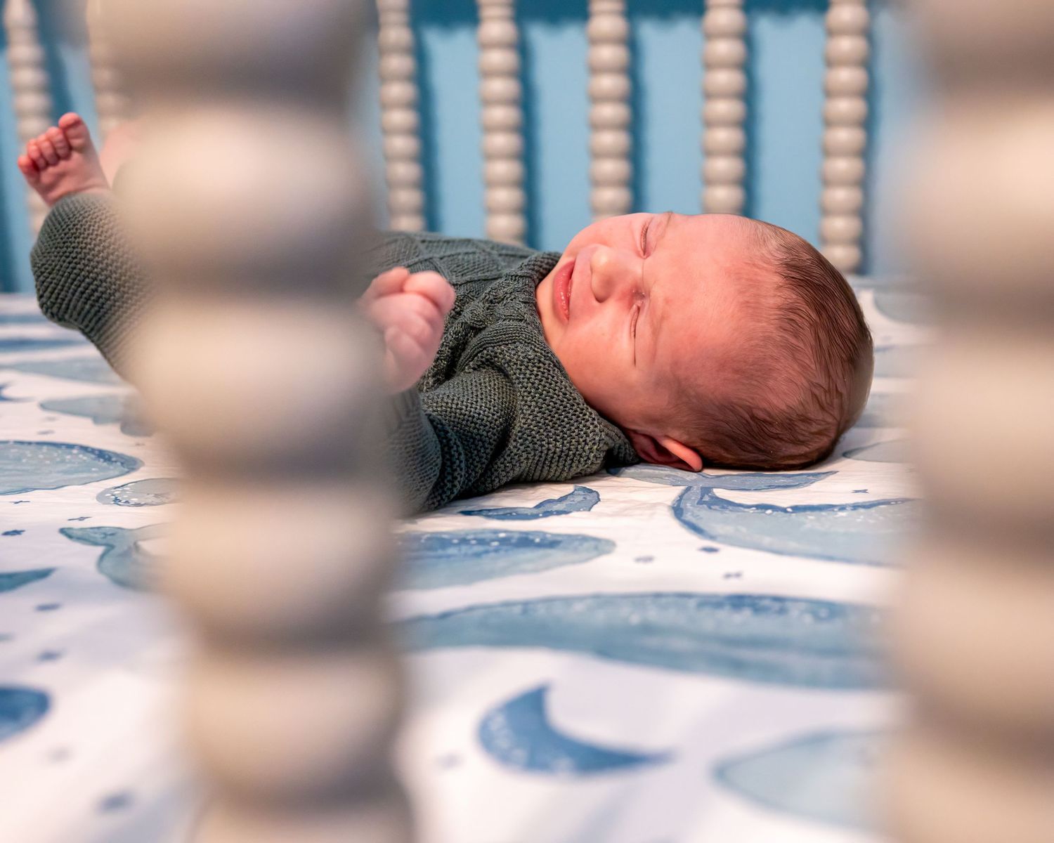 A newborn baby lying on a blue and white patterned blanket stretches and yawns.