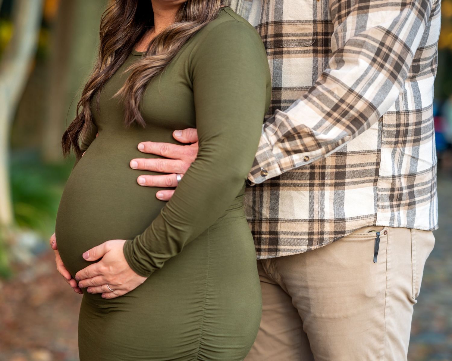 A close up of Luna's pregnant belly with her husband holding her from behind