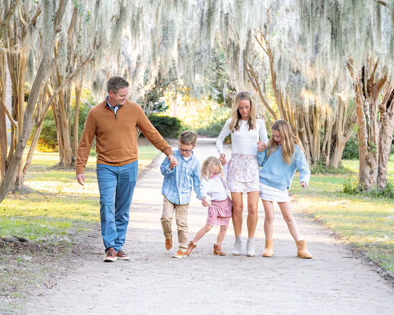 People walking casually along a winding dirt path under Spanish moss draped trees.