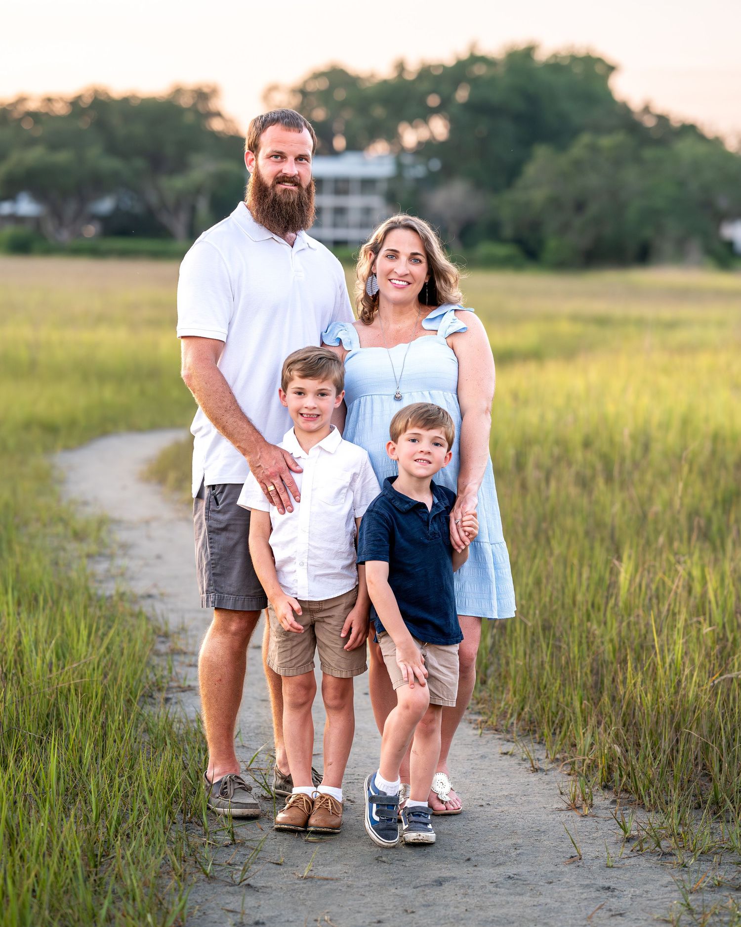 A family stands together on a path through coastal marsh grass at sunset.