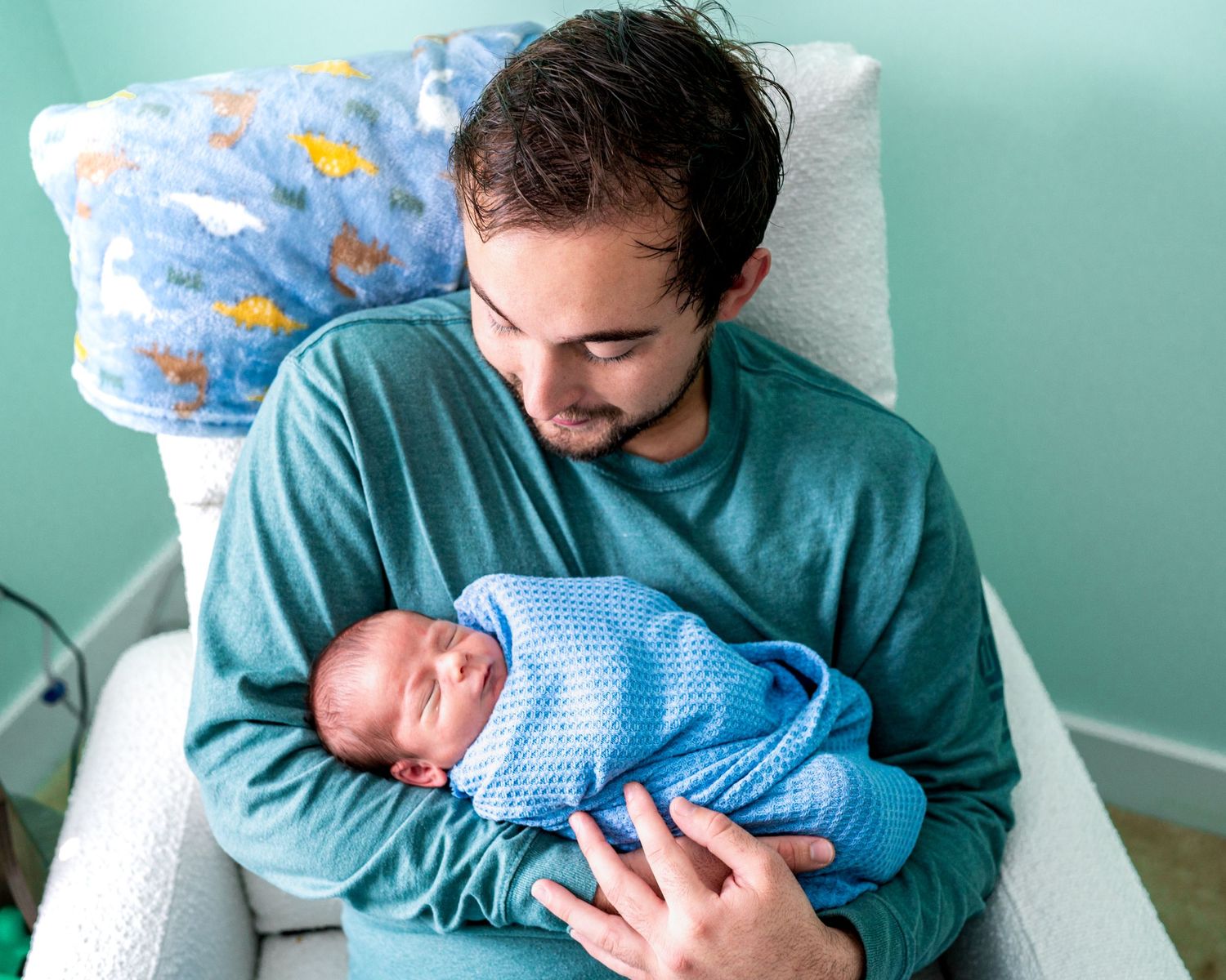 Parent in teal shirt holding newborn baby wrapped in blue swaddle.