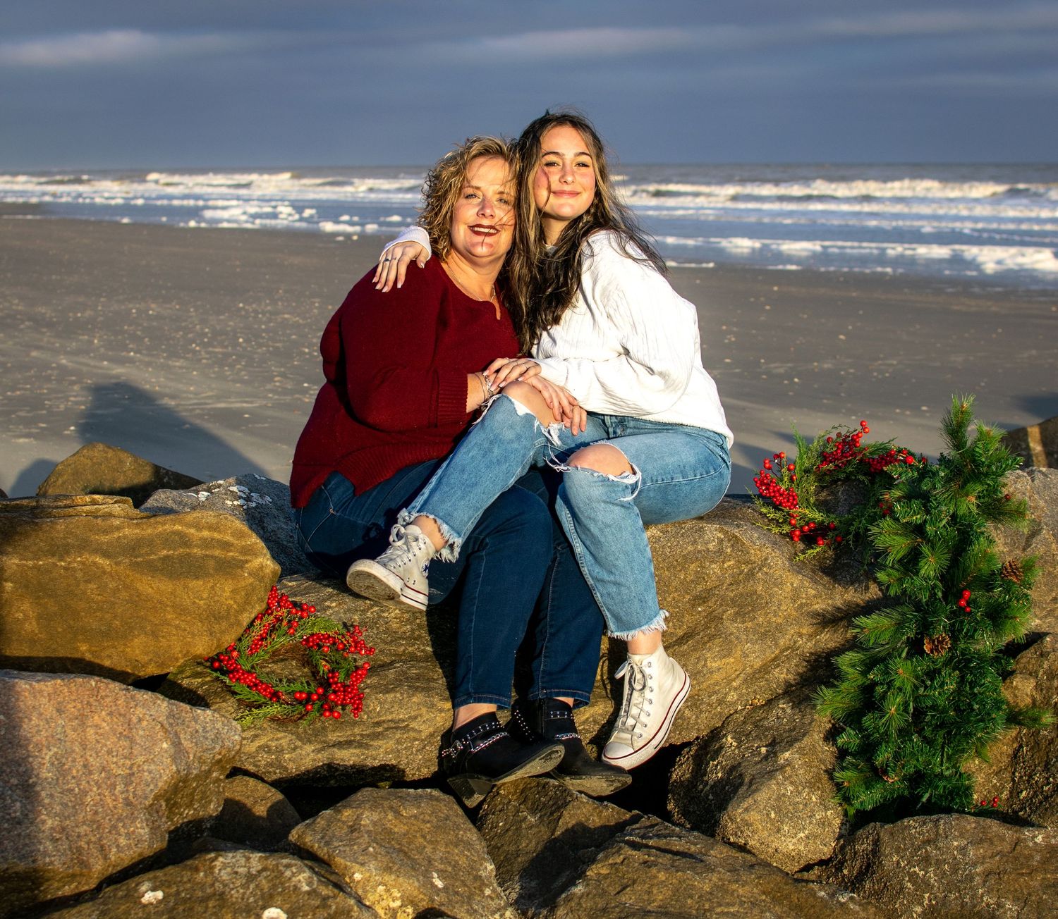 Mom and teenage daughter sitting on rocks at the beach bathed in warm sunlight