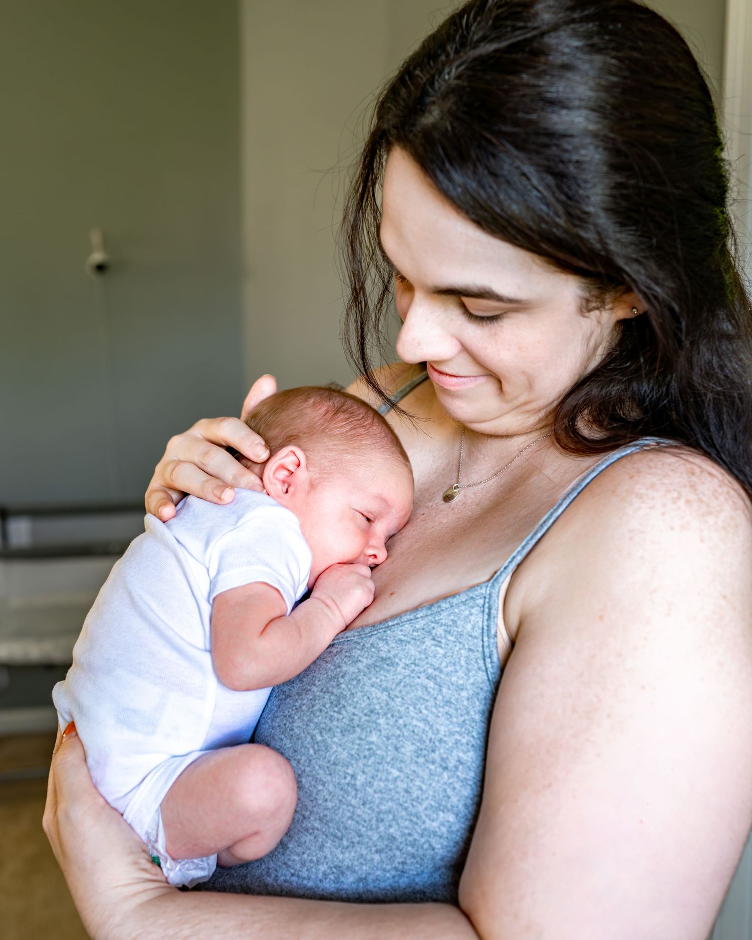 A tender moment between parent and newborn baby dressed in white against a gray background.