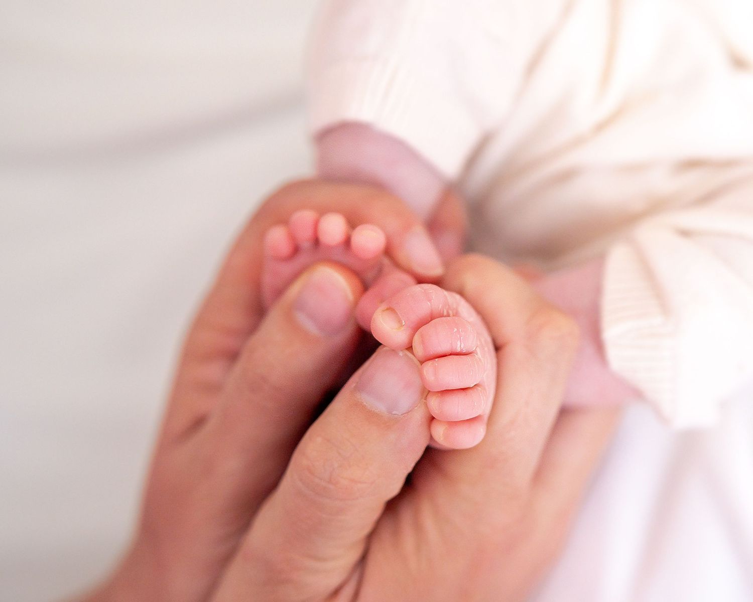Close-up of newborn baby's tiny feet being gently held by parent's hands.