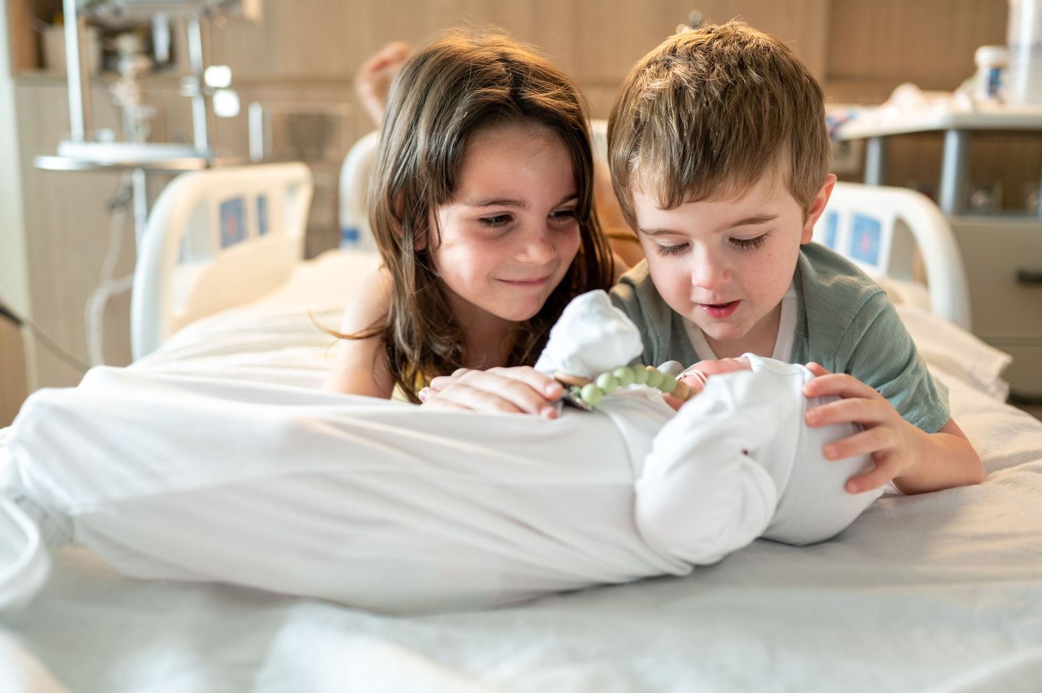 Kelly and tom lay on their stomachs in their mother's hospital bed as they meet their new baby brother during their family Fresh48 session