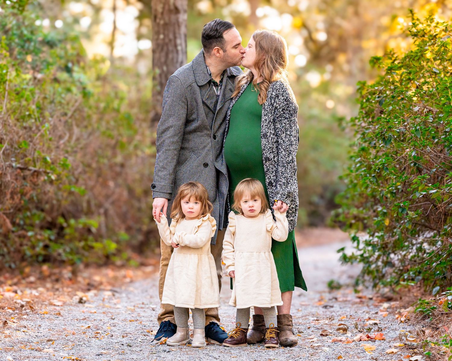 A loving family enjoying a tender moment together on a path covered with autumn leaves during a fall maternity photoshoot.