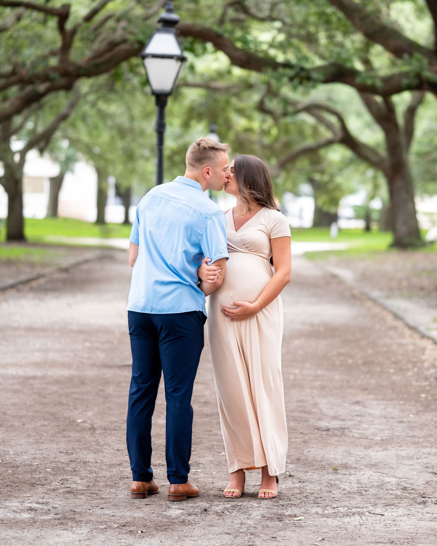 Husband faces away from camera and pregnant wife faces the camera kissing