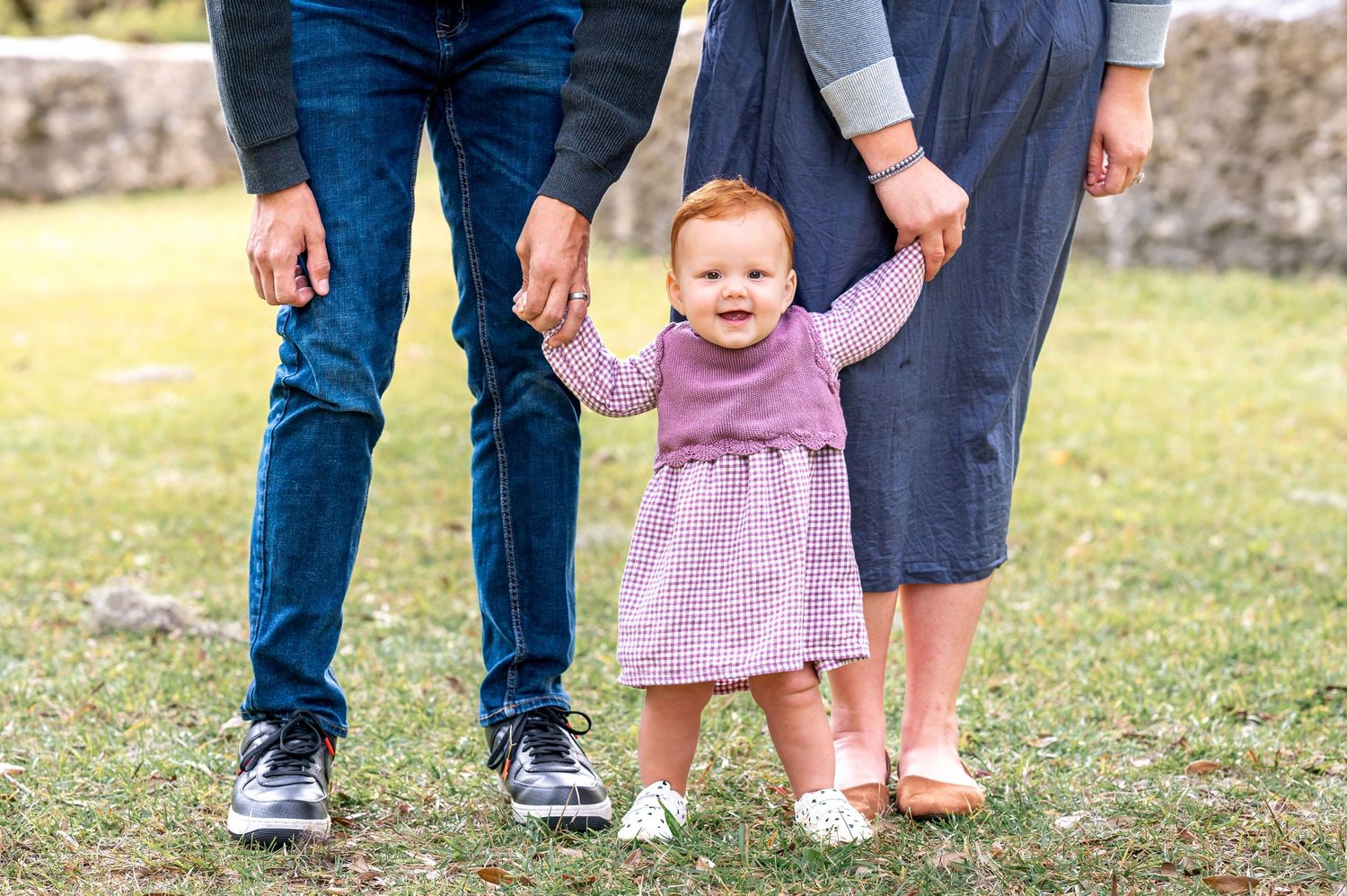 Lower body view of family members standing together on grassy ground in casual attire.