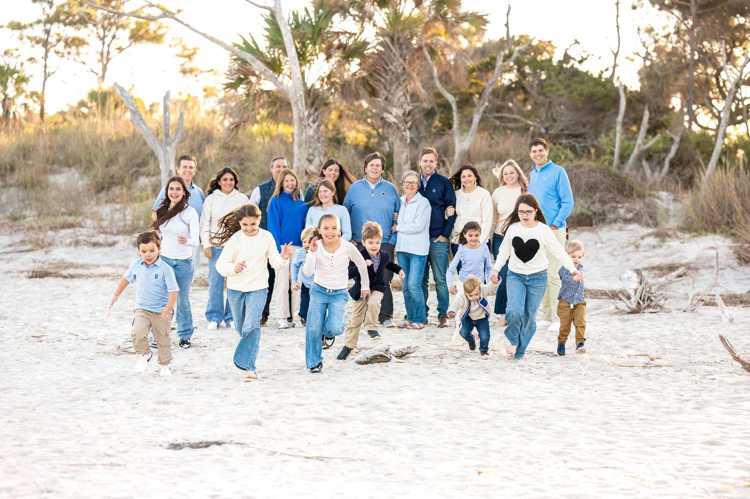 Extended family group in coordinated blue outfits posing together on beach sand.