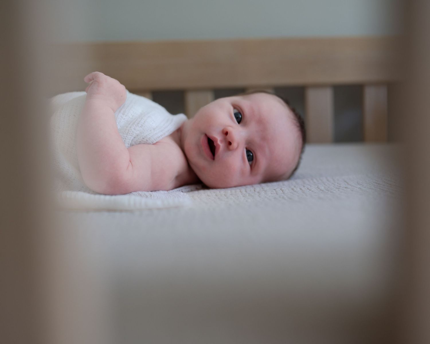 Newborn little girl, swaddled, laying awake in her crib. photo taken through the crib slats
