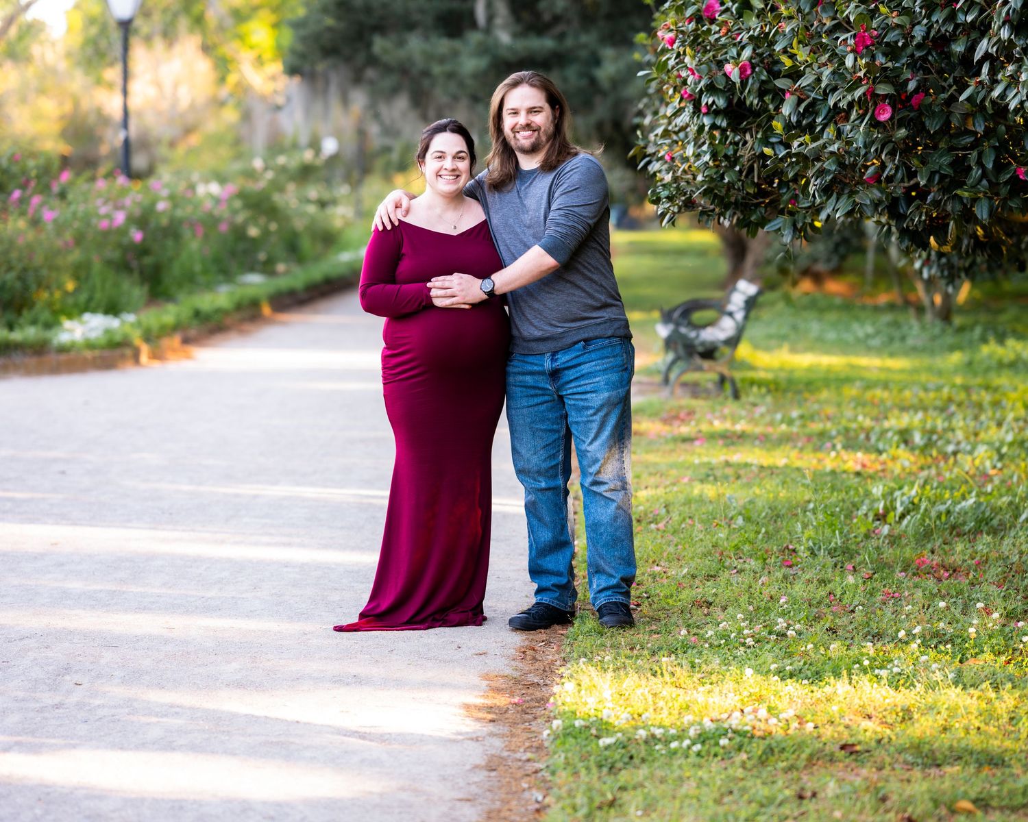 A couple poses together on a park pathway surrounded by autumn foliage and gardens.