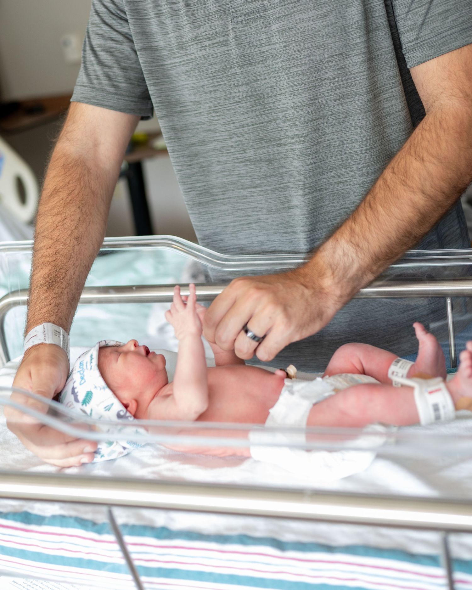 Newborn boy cries in his hospital bassinet as his father tries to soothe him.