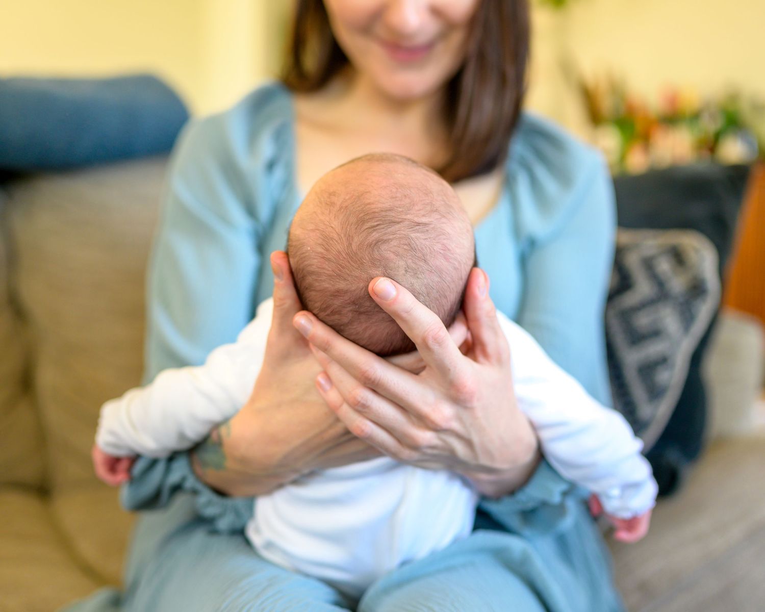 Tender moment with a newborn baby being cradled by his mother. Baby is wearing white and the mother is in a soft blue dress.