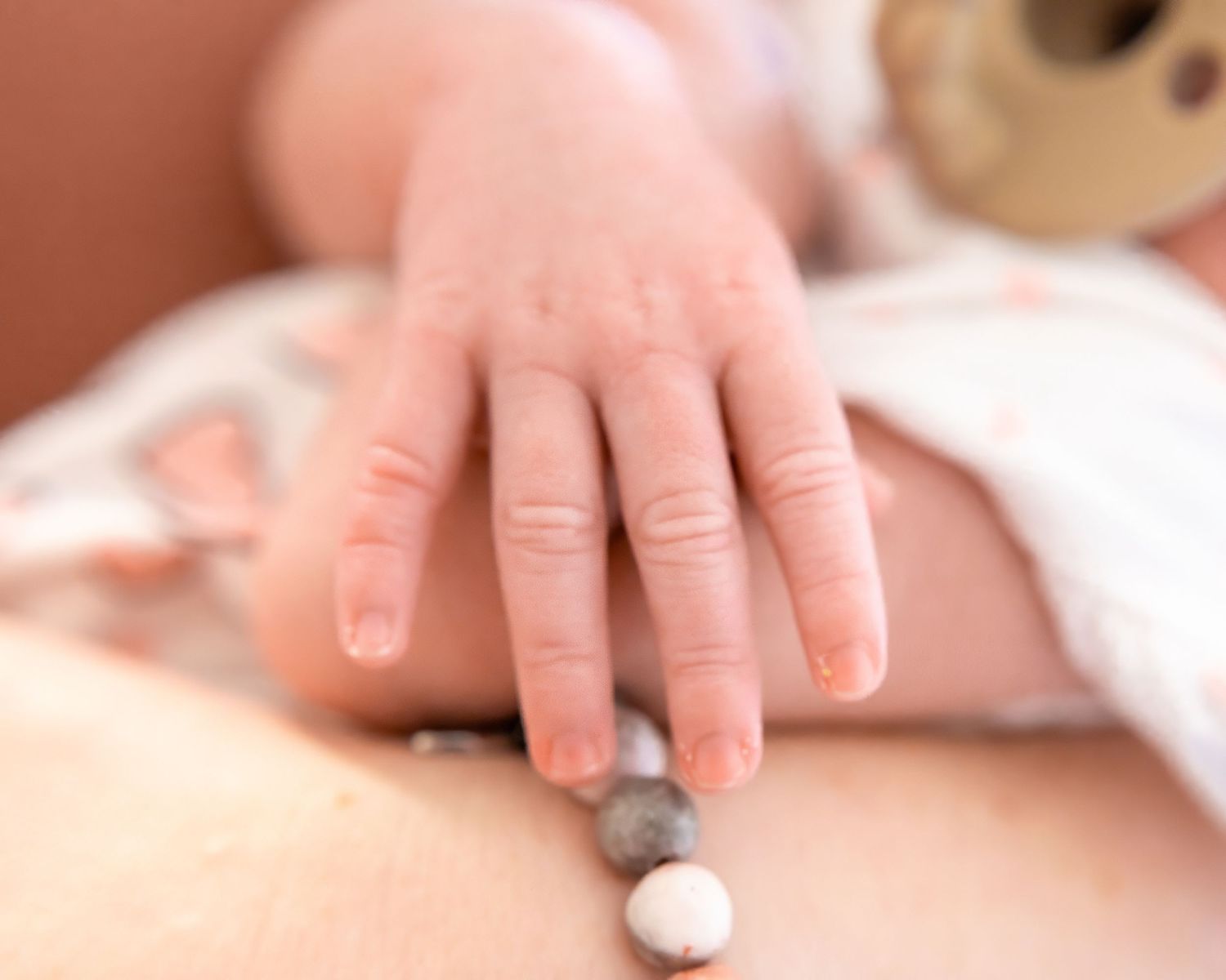 A tiny baby's hand reaches out to touch a small white and grey object on a soft surface.