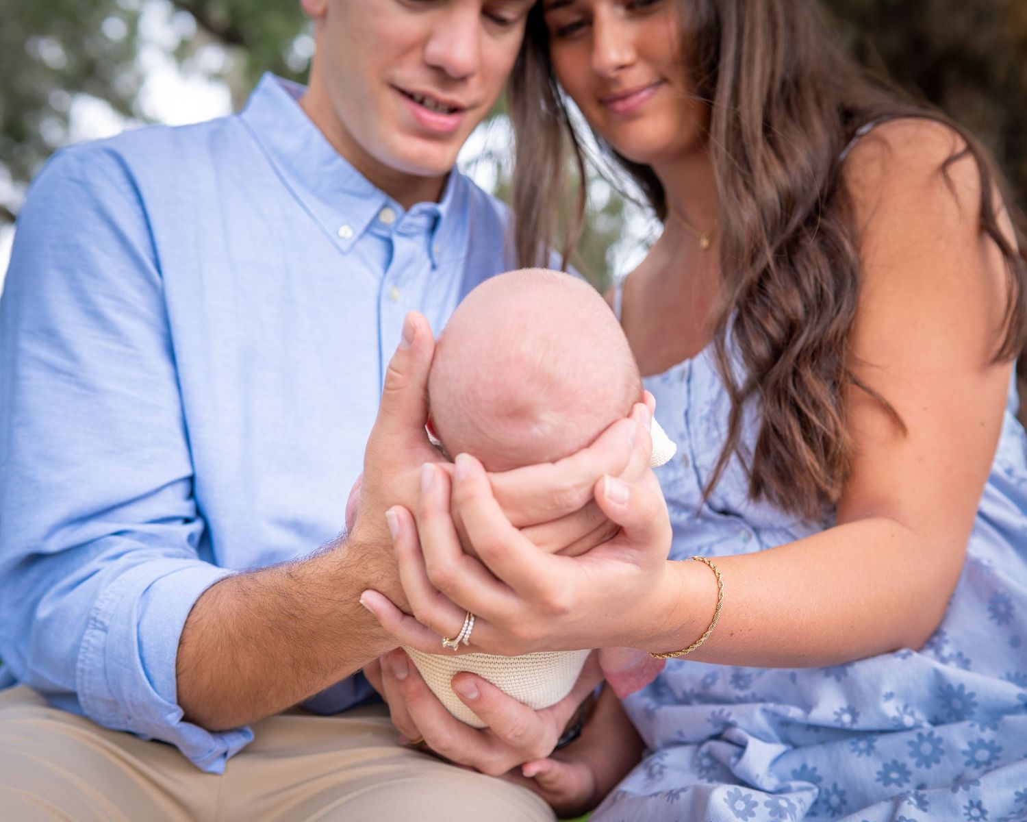 Cropped photo of mom and dad sitting side by side holding their newborn son between them, each cradling his head