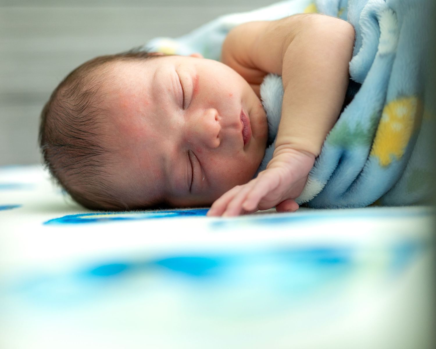 A peaceful sleeping newborn rests on soft blue blanket with yellow accents.