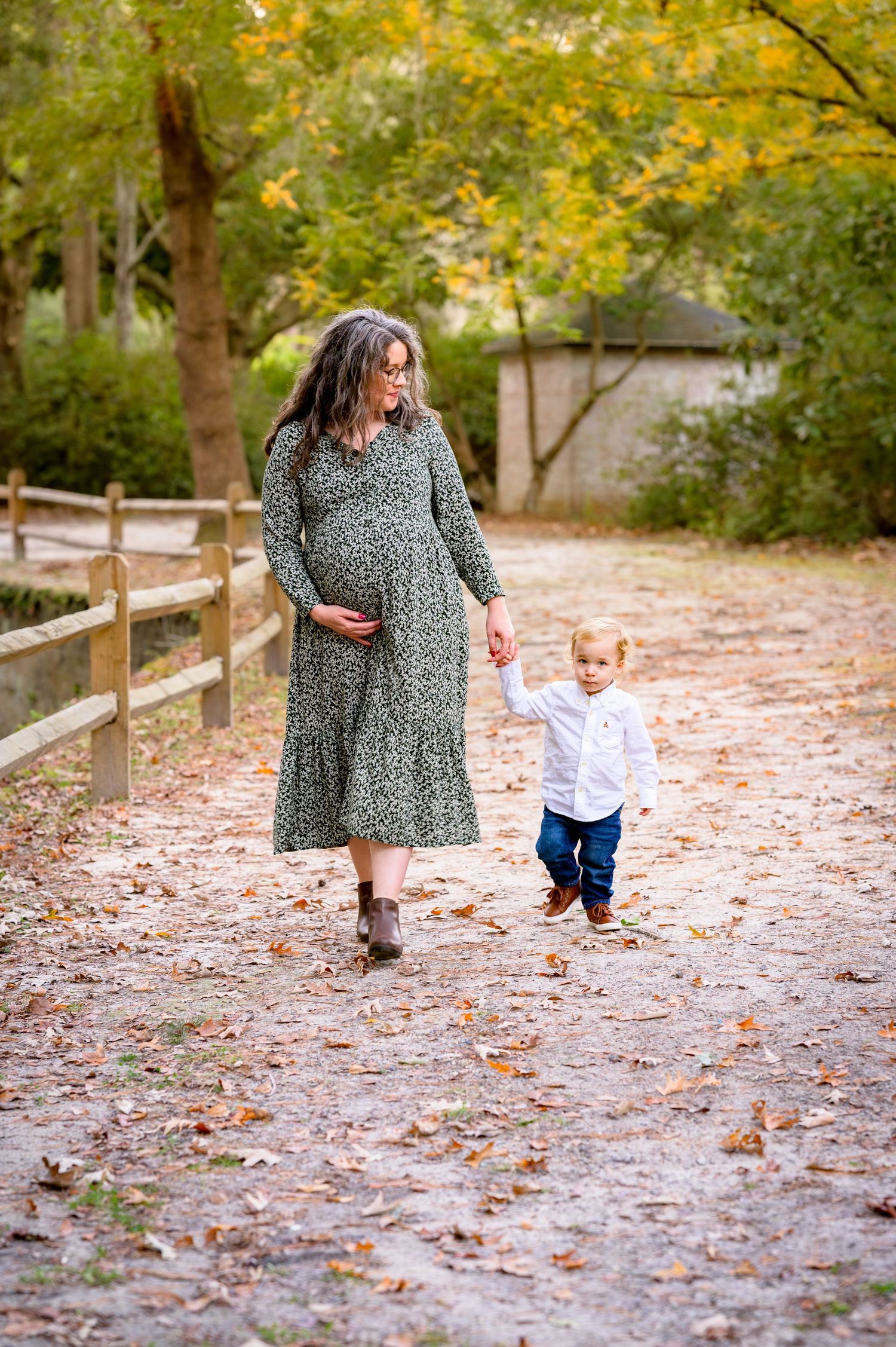Erin holds her toddler son's hand with one hand and her pregnant belly with the other as they walk through Azalea Park