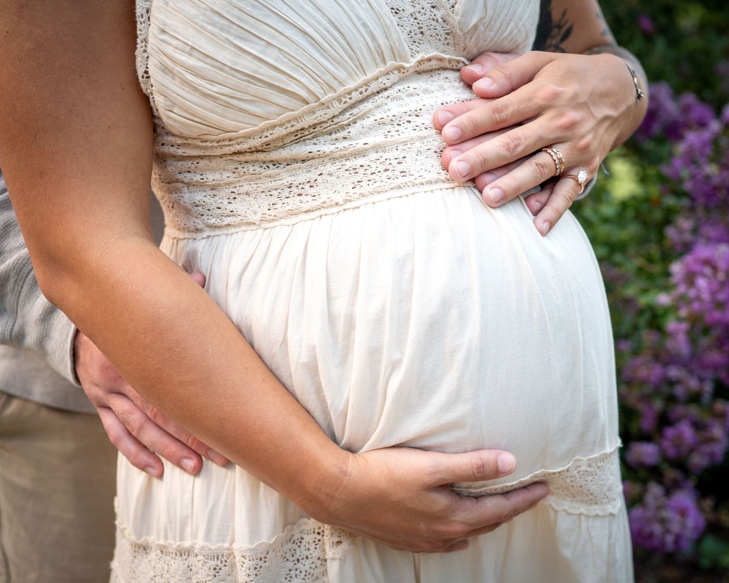 Close-up detail of hands cradling a pregnant belly in a cream-colored maternity dress.