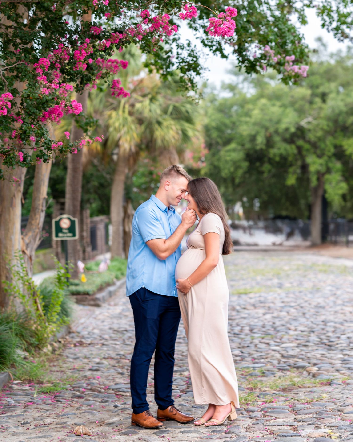A romantic moment captured under blooming pink flowers on a cobblestone path.