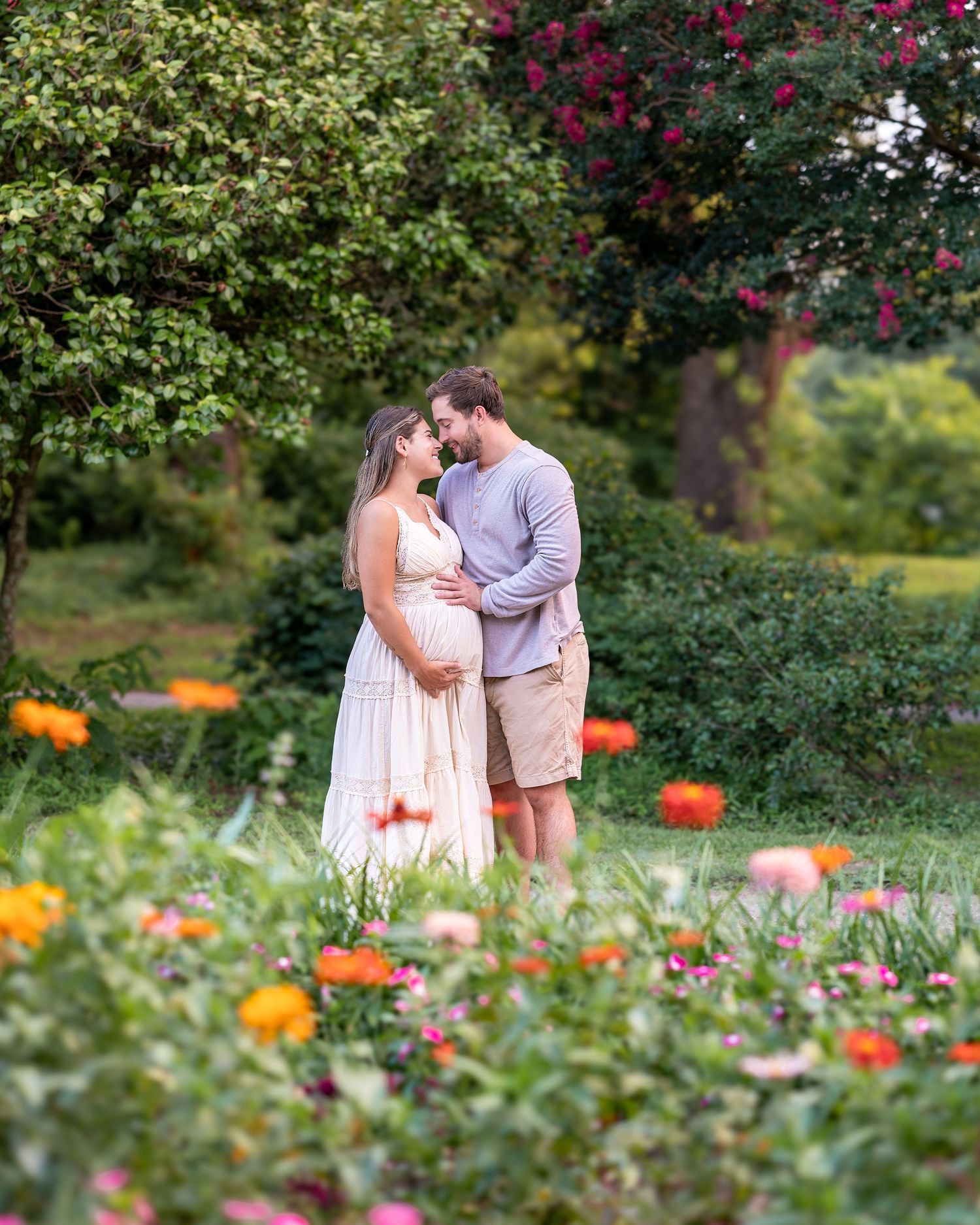 A romantic expecting couple shares tender moments in a blooming garden with orange and pink flowers during their maternity session.