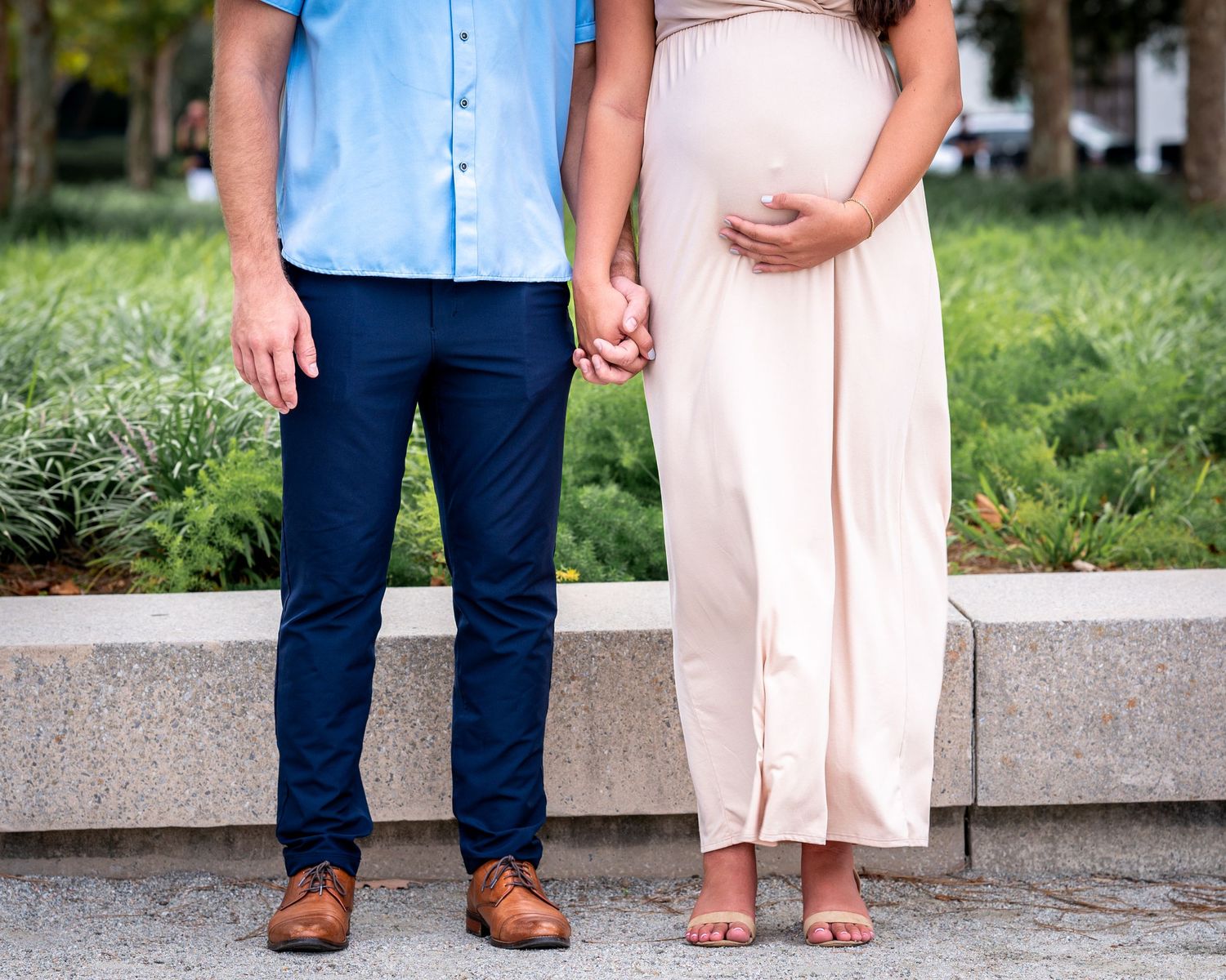 Husband and wife standing side by side holding hands, wife holding baby bump