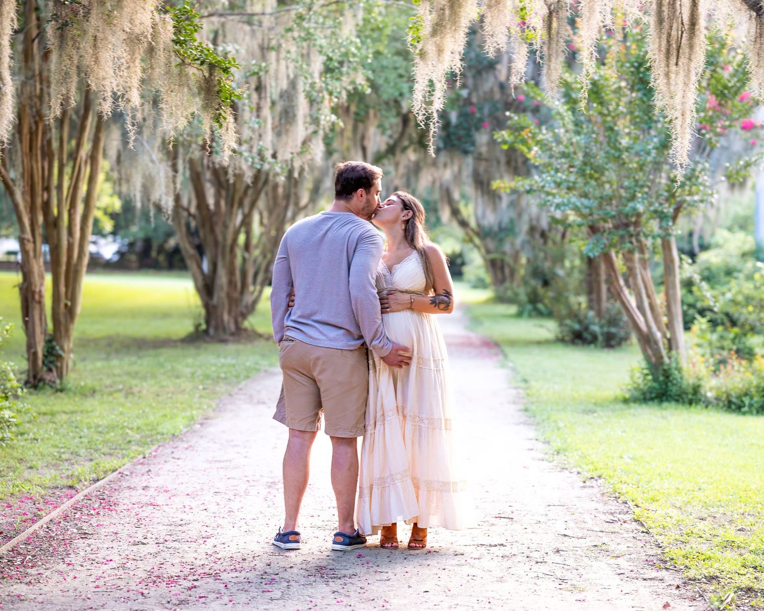 Lola and her husband stand along a path at Hampton park kissing during their maternity session