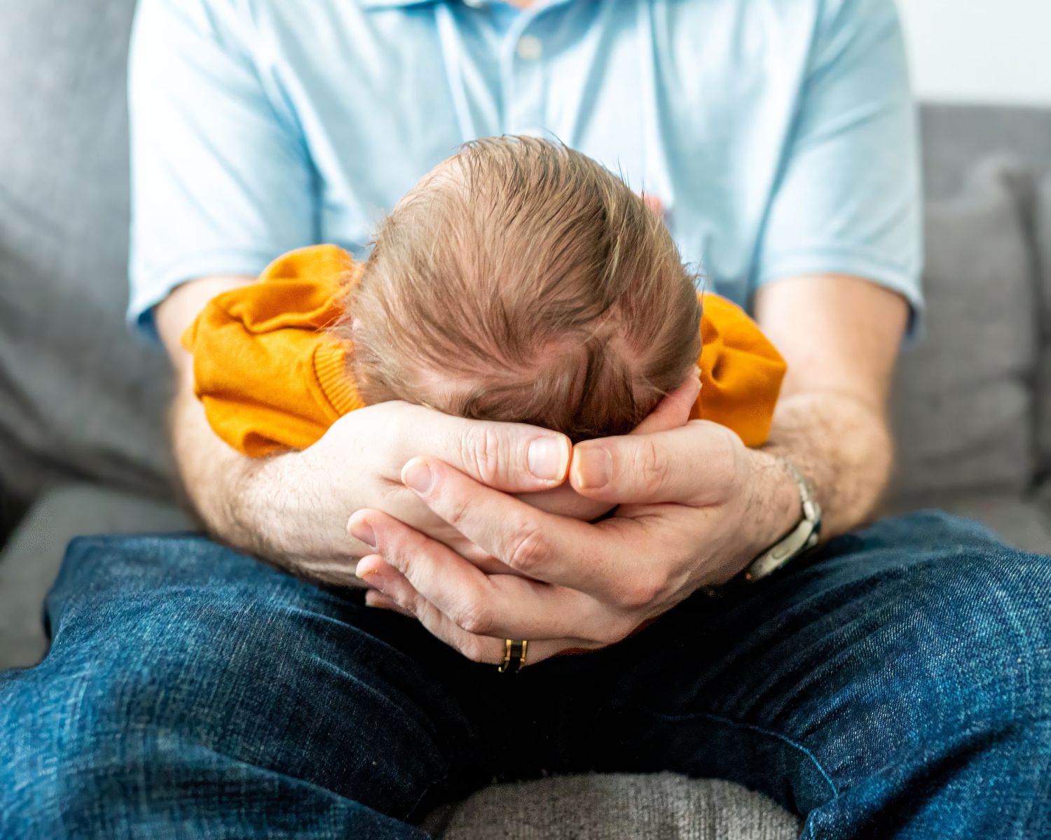 A newborn baby sleeps peacefully while cradled in gentle hands wearing a bright orange sleeper.