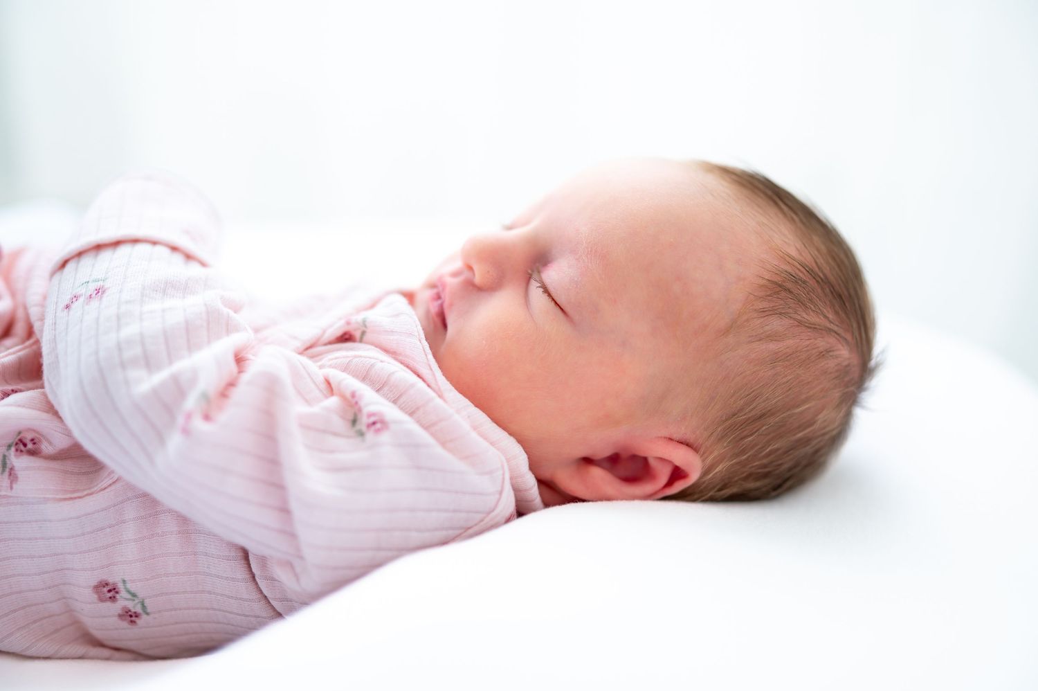 Peaceful newborn baby sleeping soundly, wrapped in a soft pink outfit on a white surface.