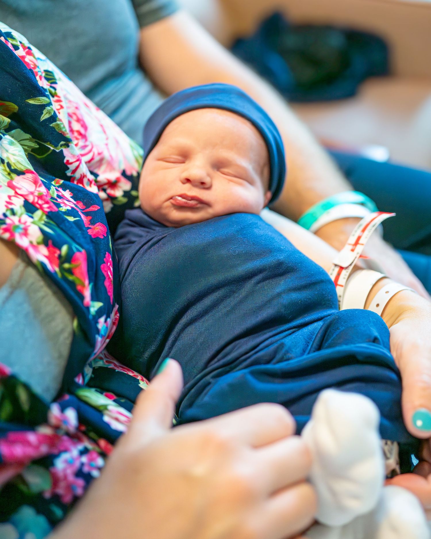 A newborn baby wearing blue sleeps peacefully while being cradled.