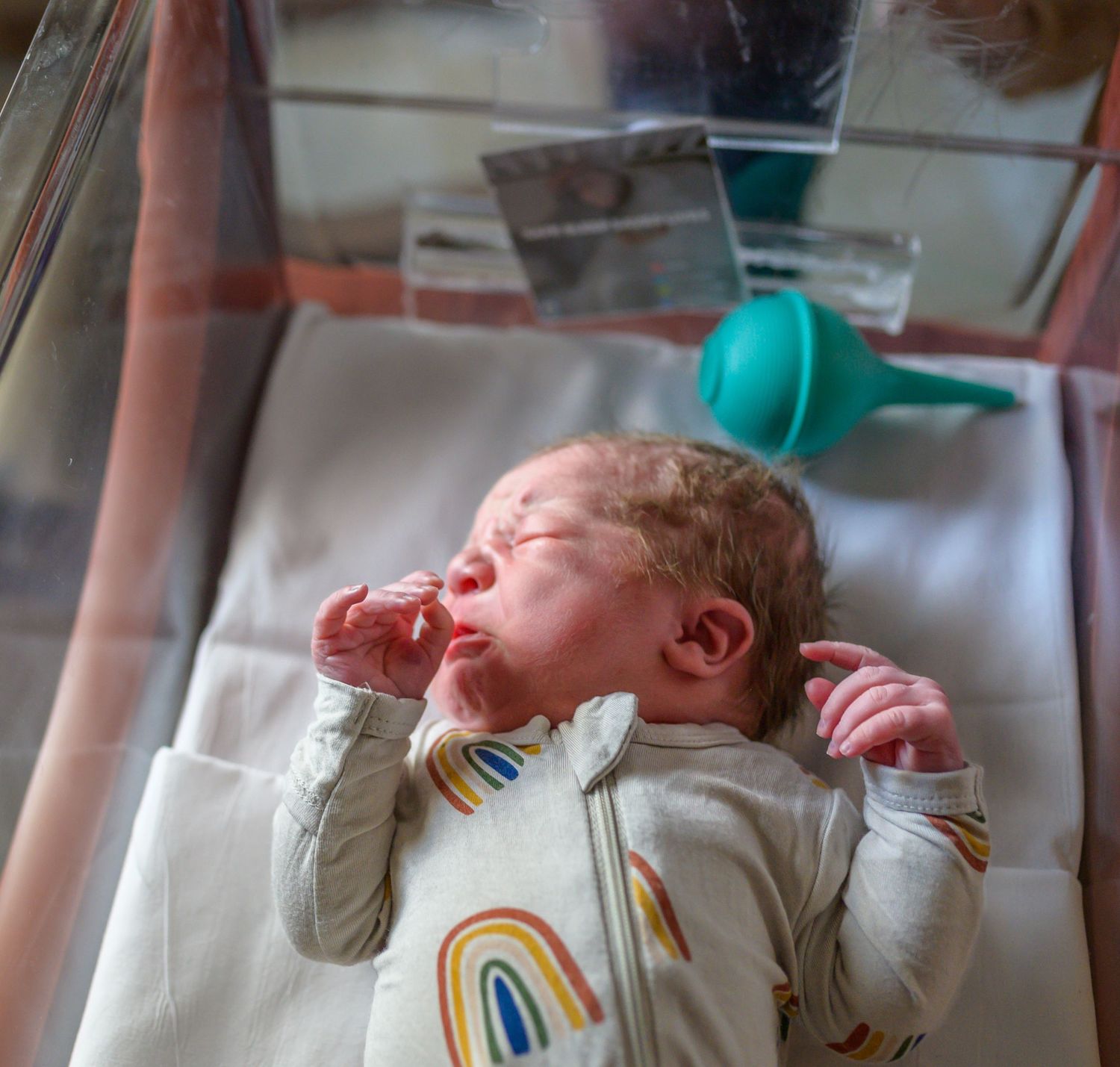 Newborn baby wearing rainbow print clothing in a hospital bassinet.