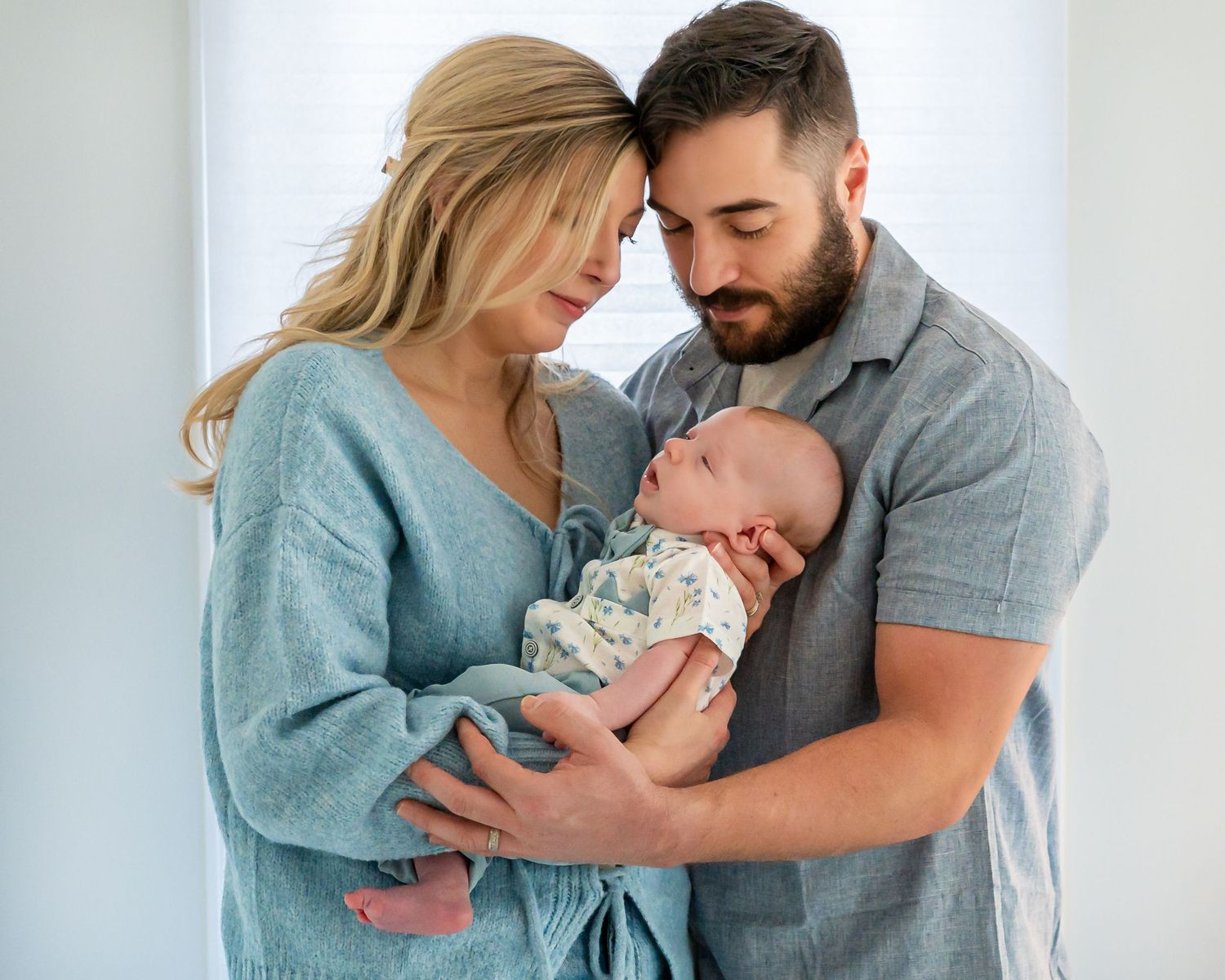 A tender family moment as parents hold and embrace their newborn baby against a light background.