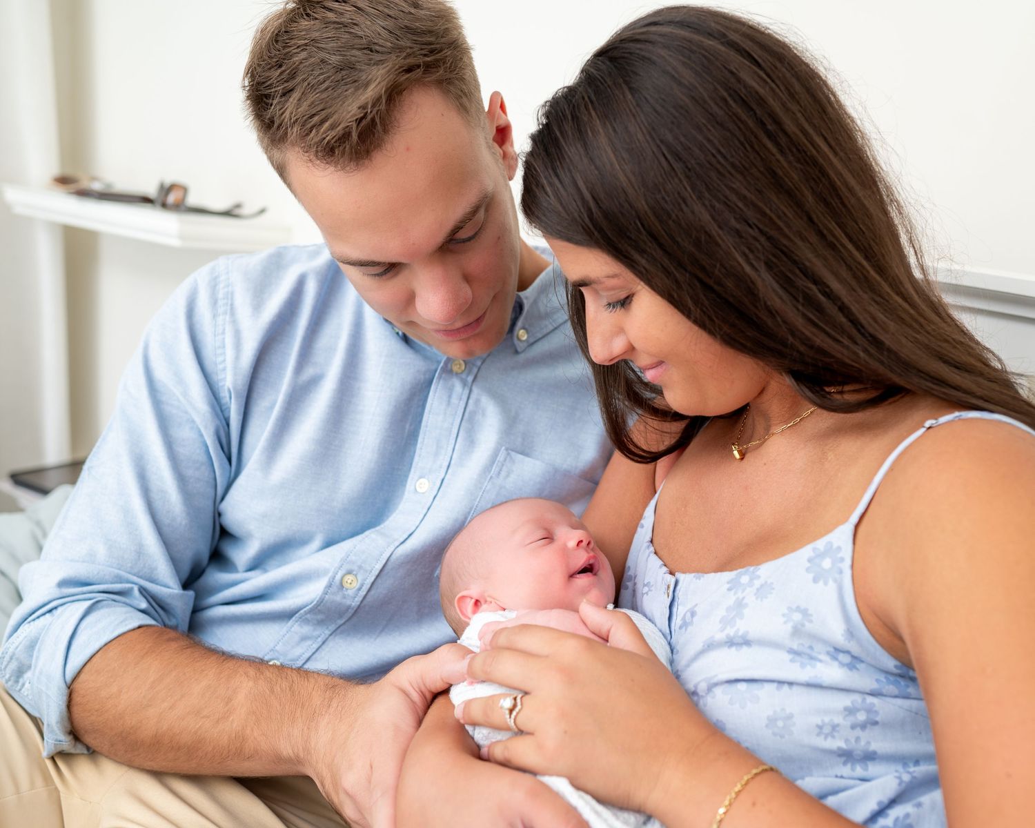 New dad and mom hold their newborn between them while sitting on bed