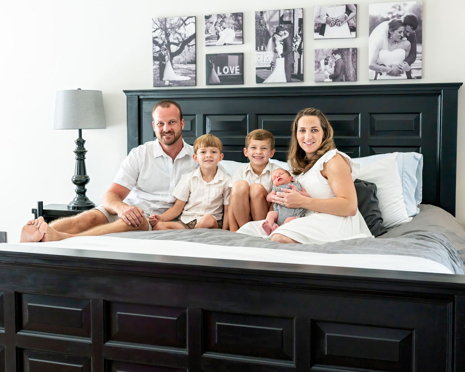 Family relaxing together on bed with dark headboard and framed photos displayed above.