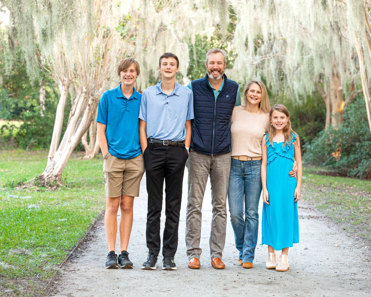 Edited Photo: A family in coordinated blue and white outfits poses together on a tree-lined path for outdoor portraits.
