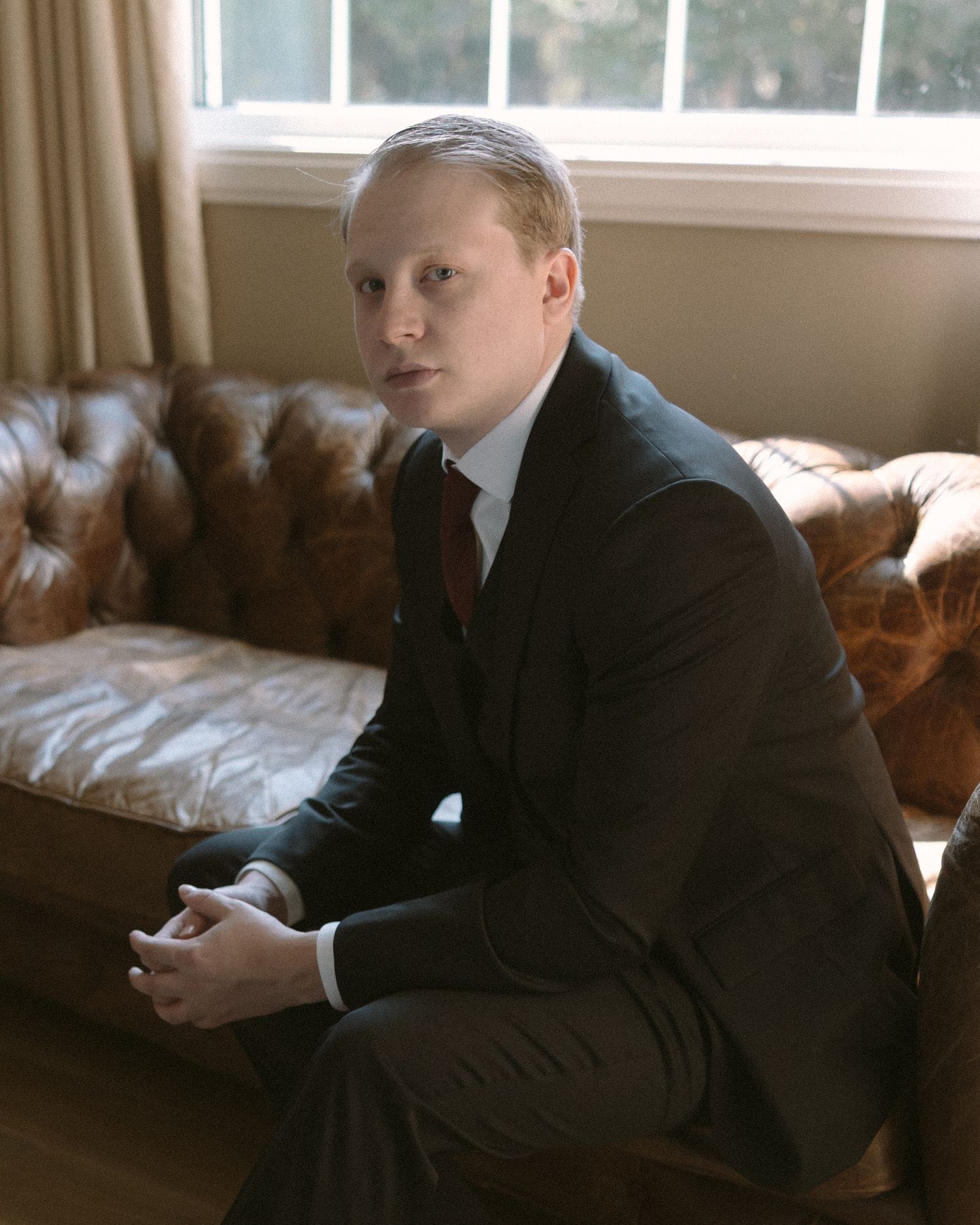 Groom standing by a window in natural light, a quiet, reflective moment before the ceremony.
