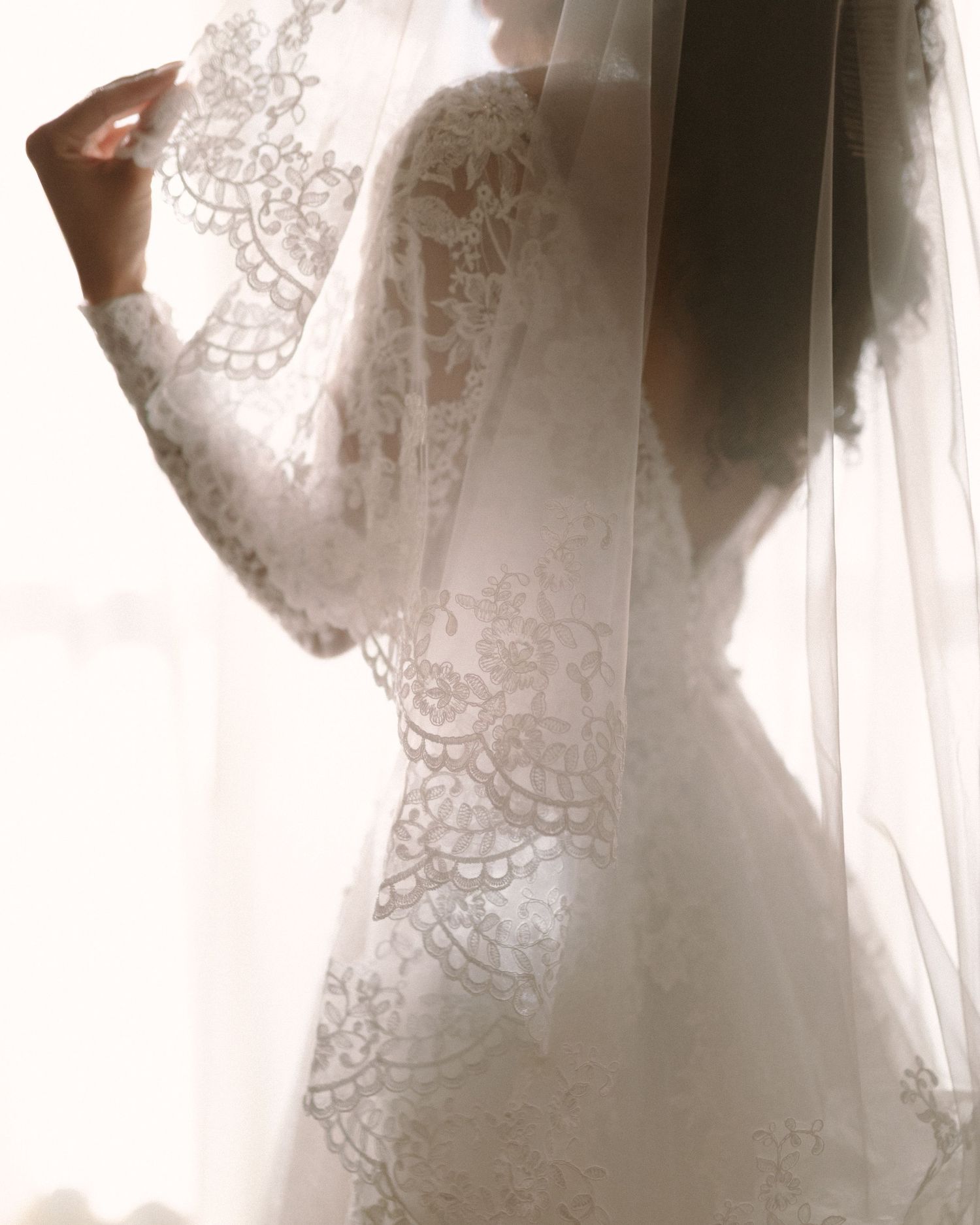 Bride in soft window light, framed through a doorway for an intimate, candid getting-ready moment.