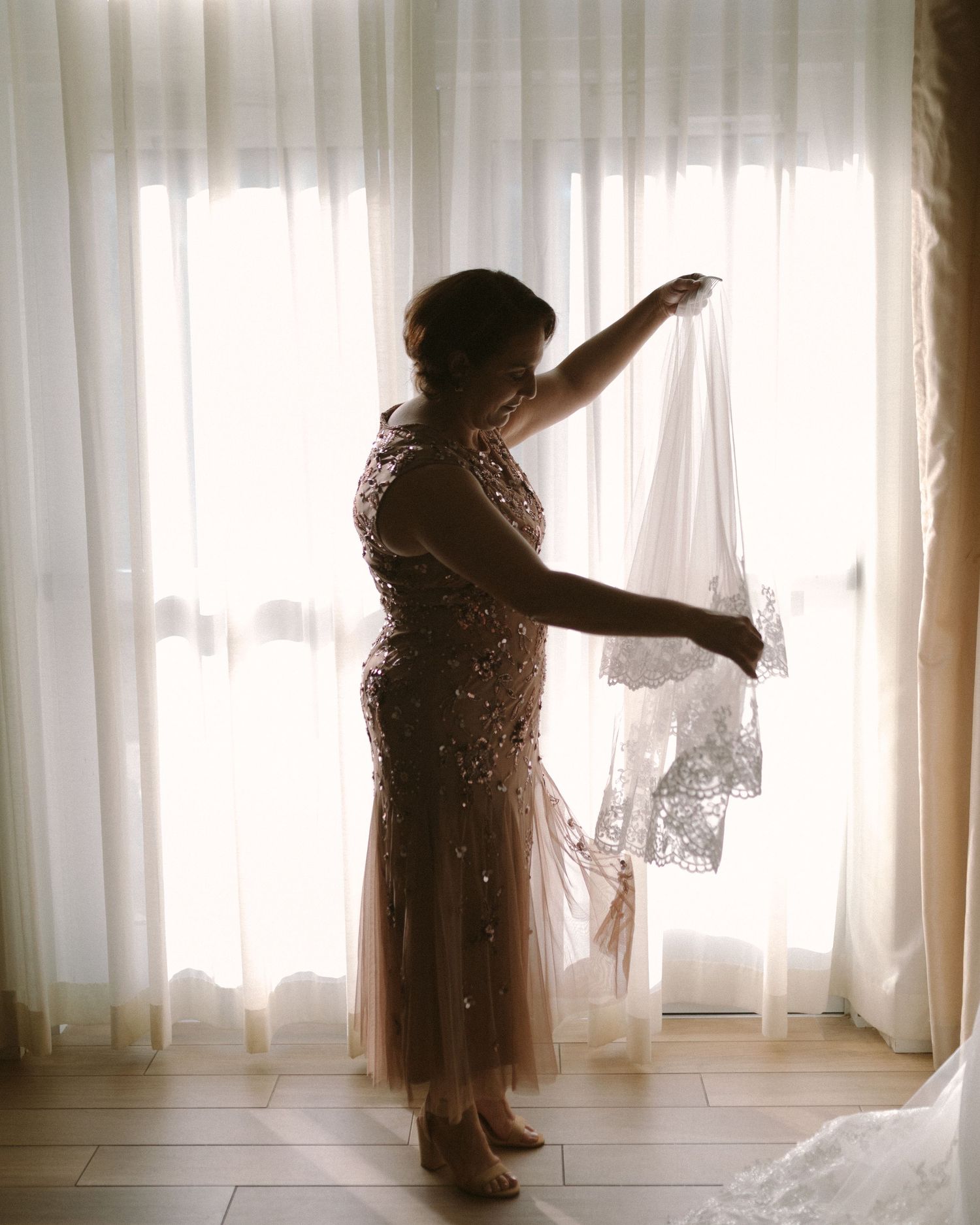 Bride in soft window light, framed through a doorway for an intimate, candid getting-ready moment.