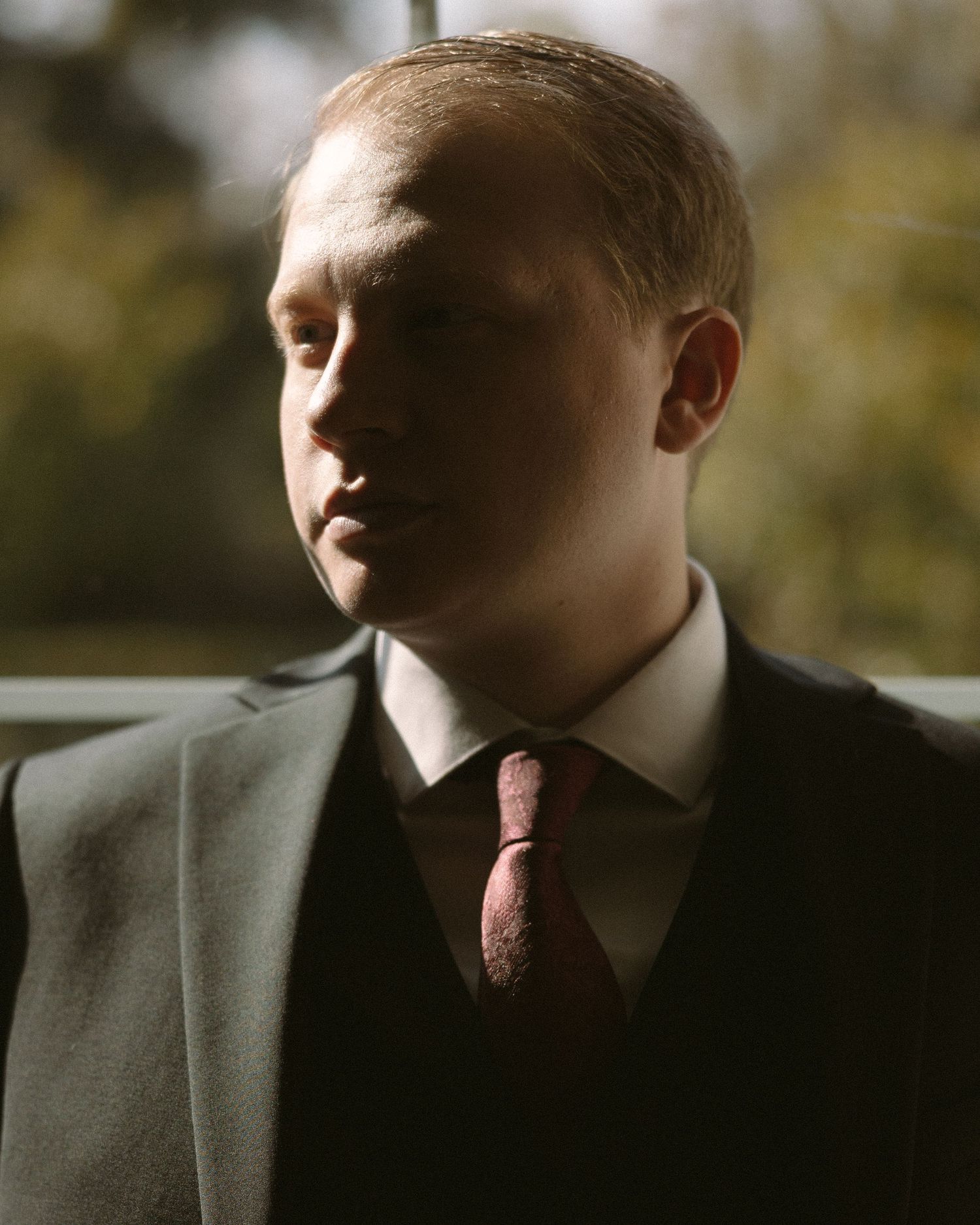 Groom standing by a window in natural light, a quiet, reflective moment before the ceremony.