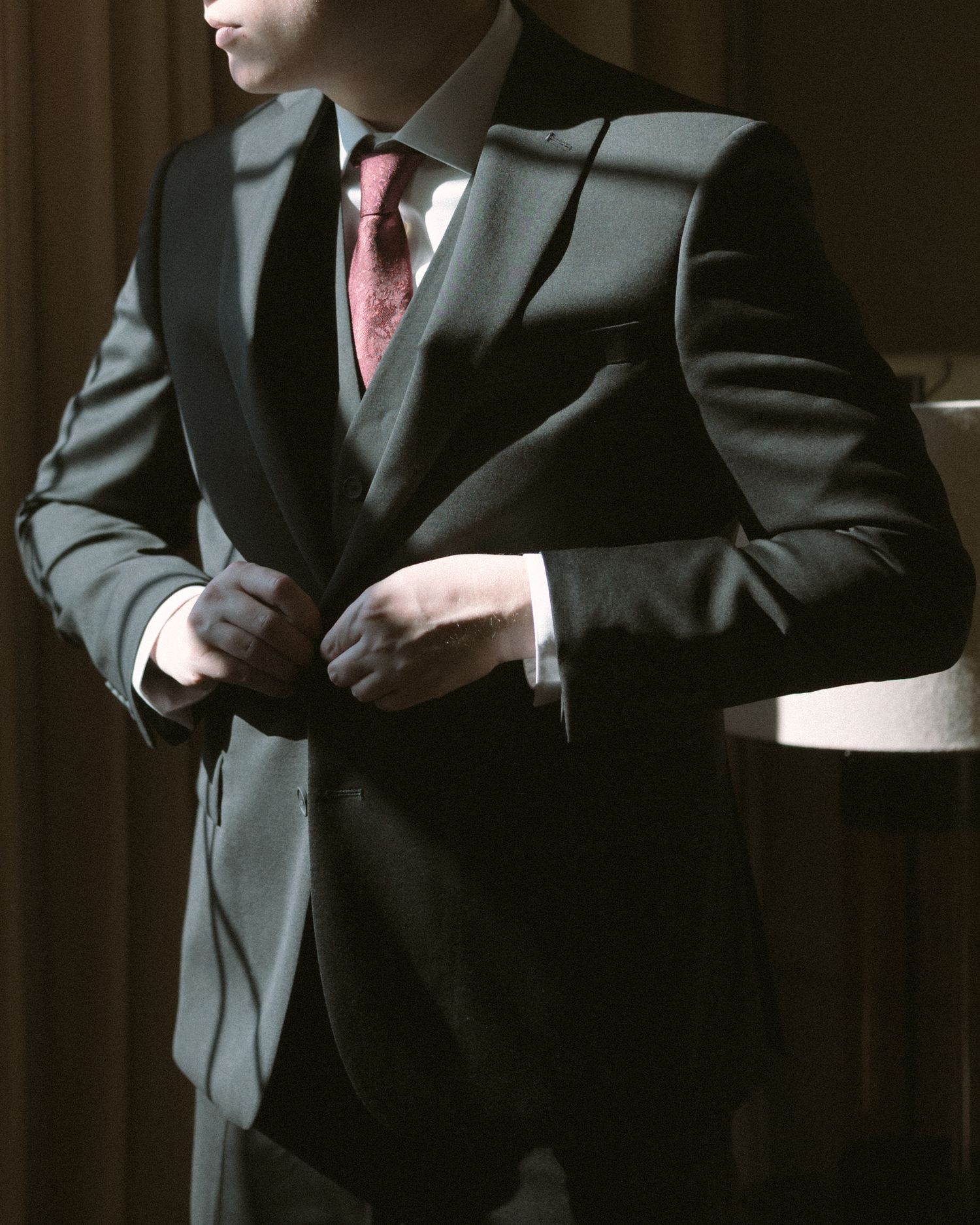 Groom standing by a window in natural light, a quiet, reflective moment before the ceremony.