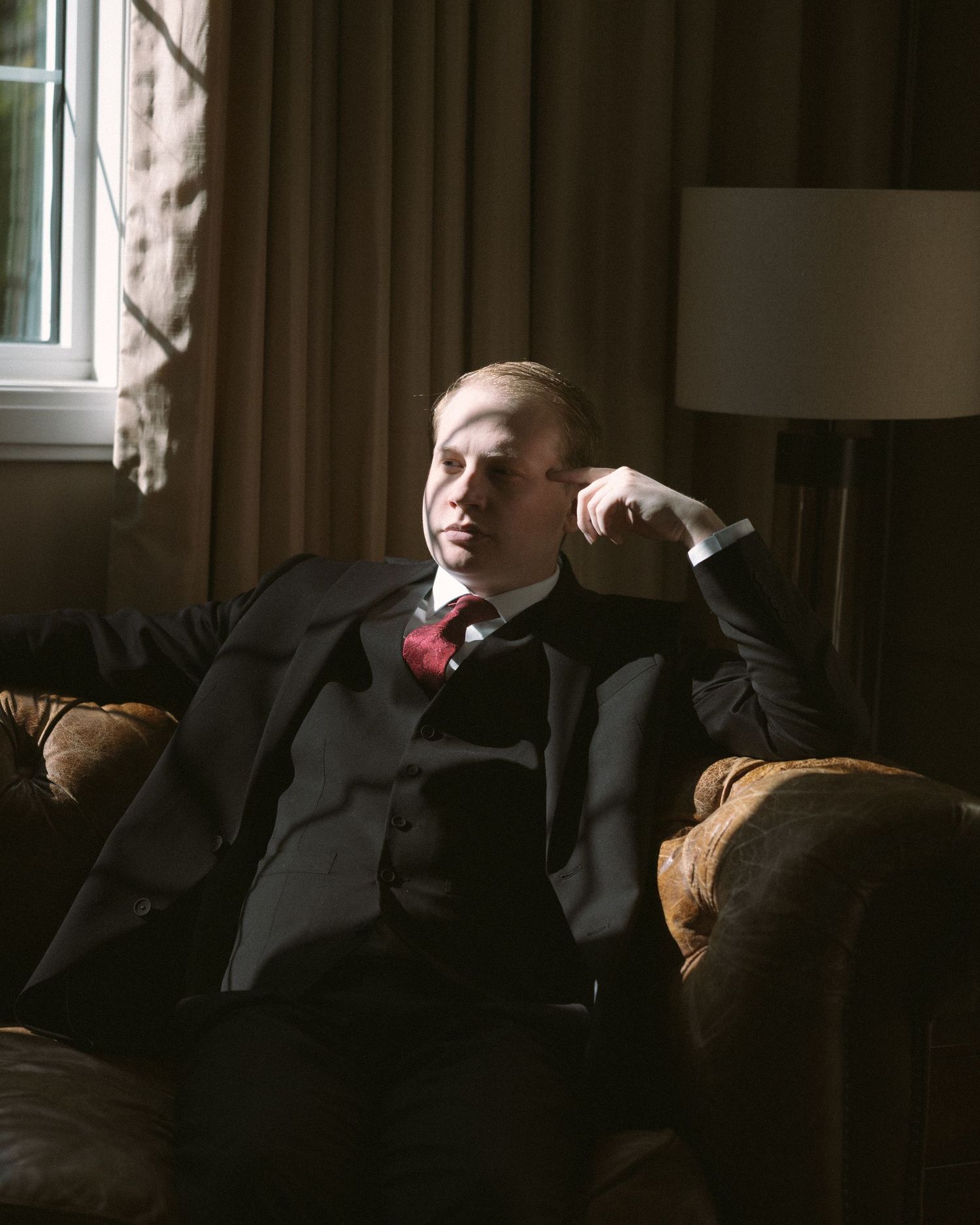 Groom standing by a window in natural light, a quiet, reflective moment before the ceremony.