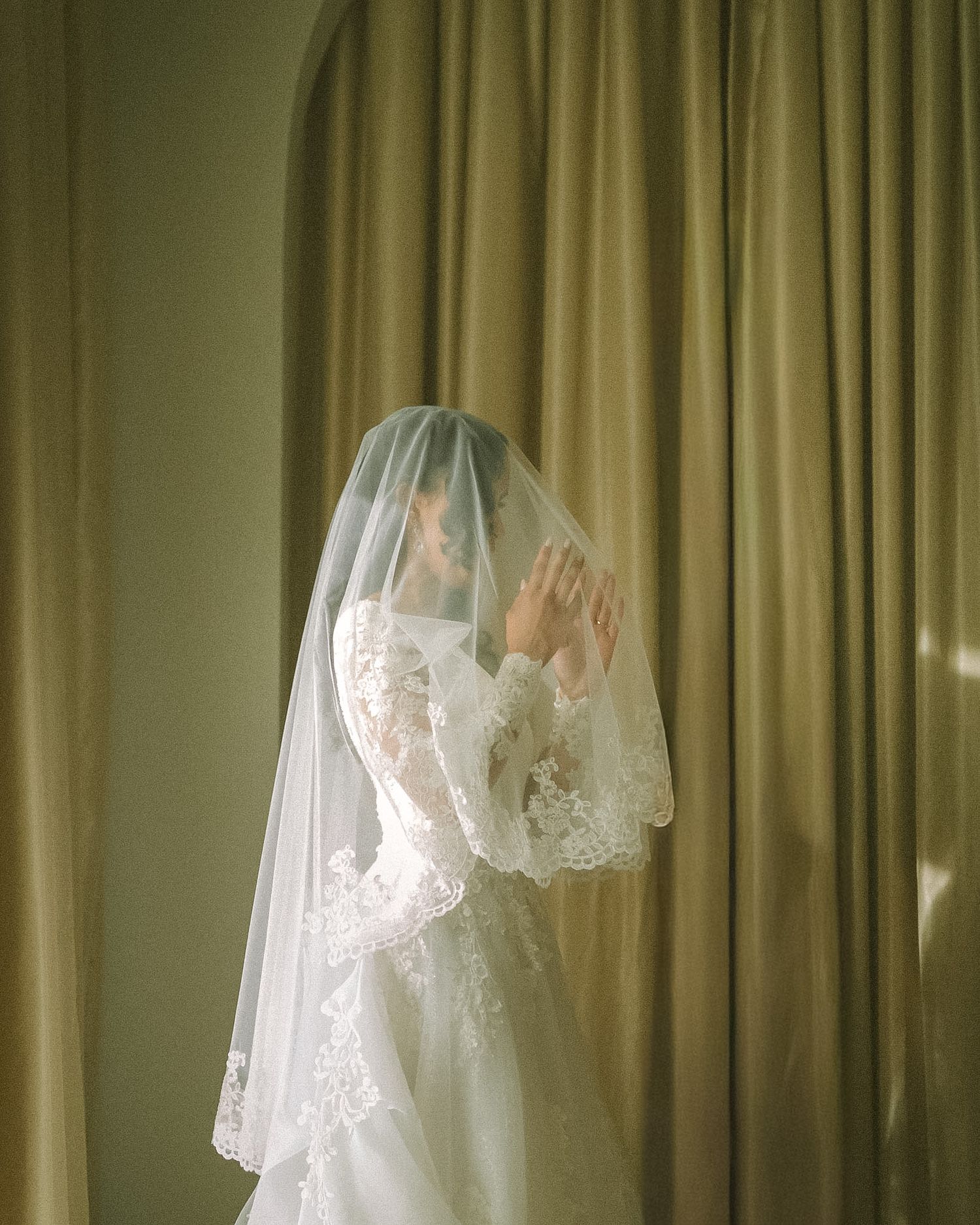 Bride in soft window light, framed through a doorway for an intimate, candid getting-ready moment.
