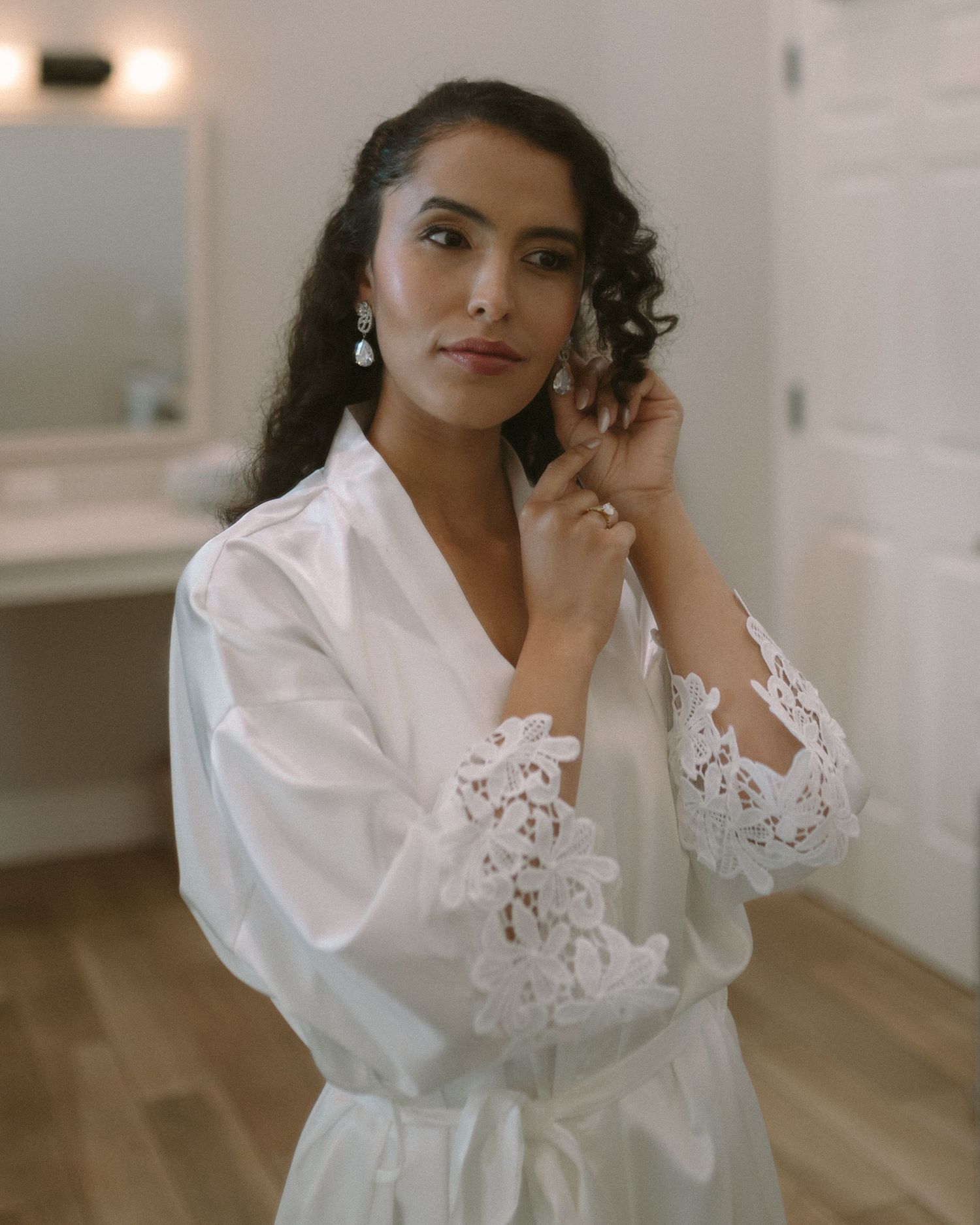 Bride in soft window light, framed through a doorway for an intimate, candid getting-ready moment.