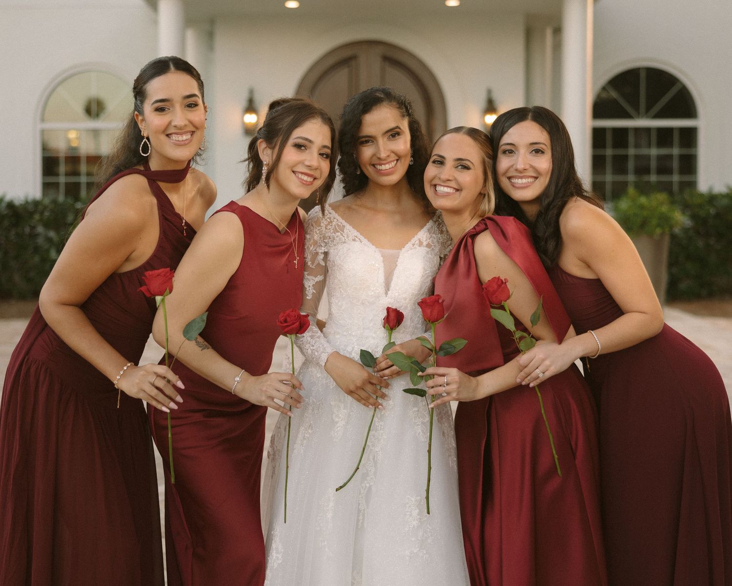 Bride surrounded by bridesmaids in coordinated dresses, smiling together in a warm, joyful group portrait.