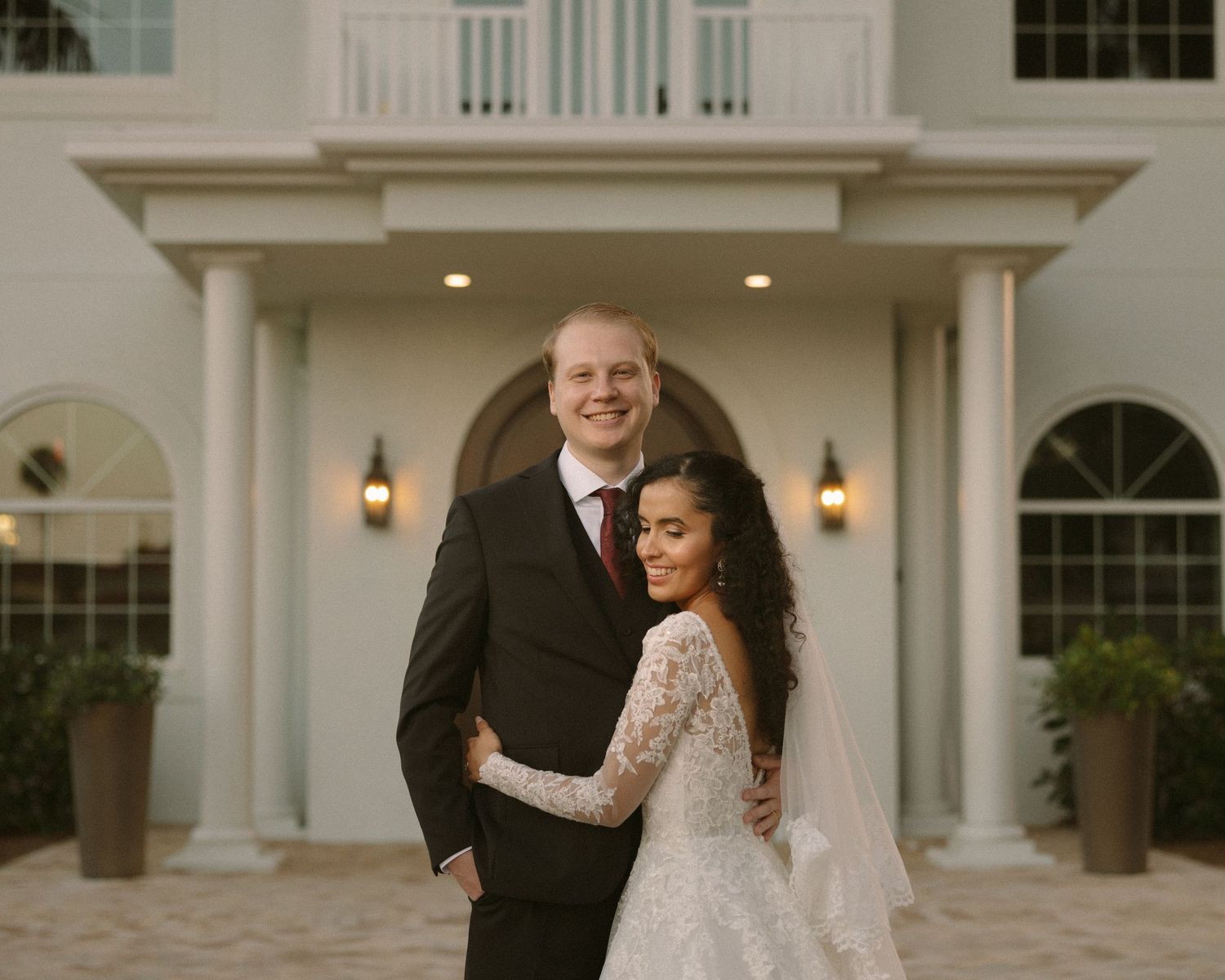 Bride and groom embrace in front of the venue, a timeless portrait with soft, natural tones.